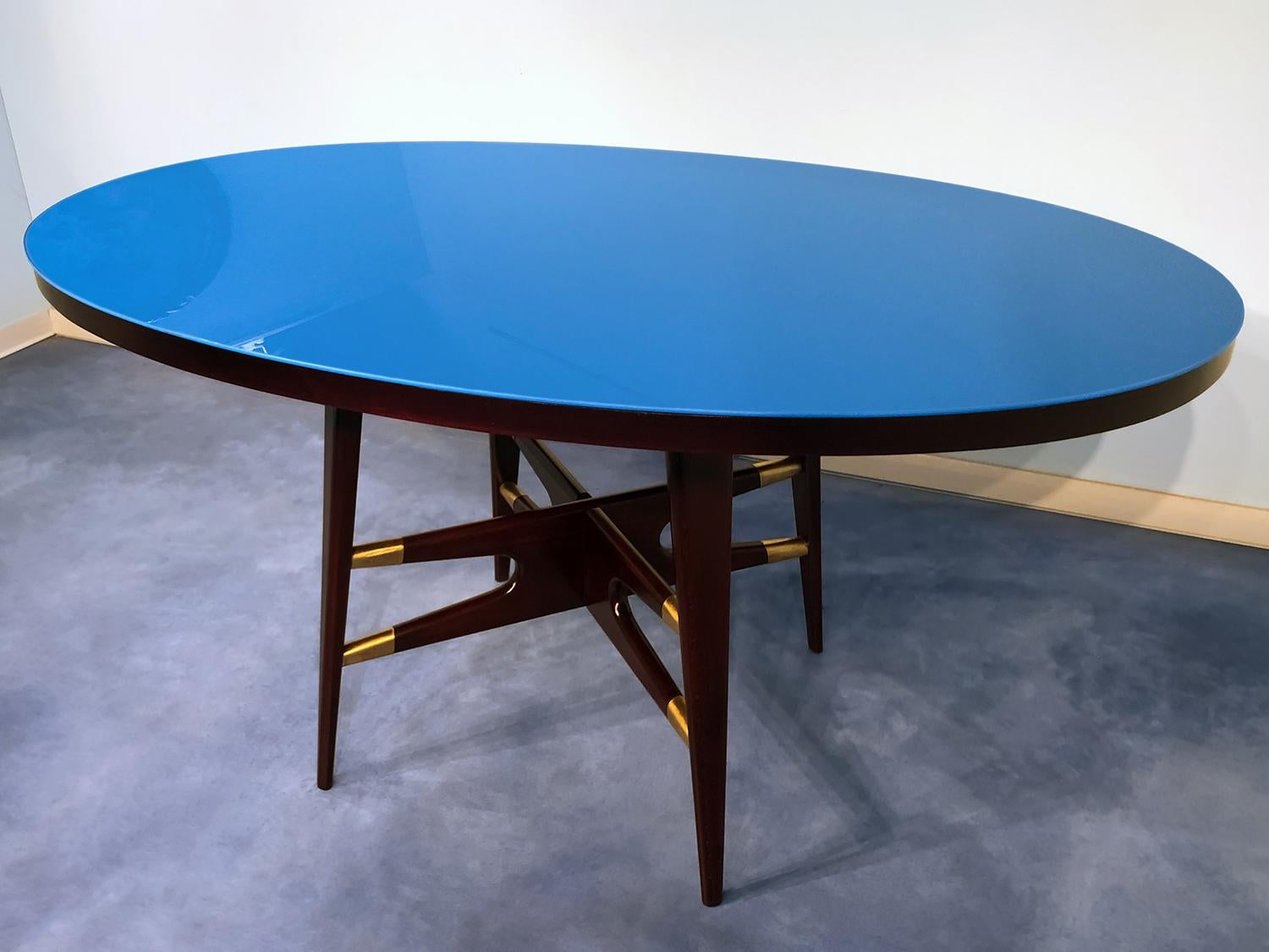 Fabulous dining table, very well designed by Silvio Cavatorta in the 1950s.
The uniqueness of its design is given by the wooden cross structure finished with fine brass details, in addition to its oval top in colored glass, which we have decided to