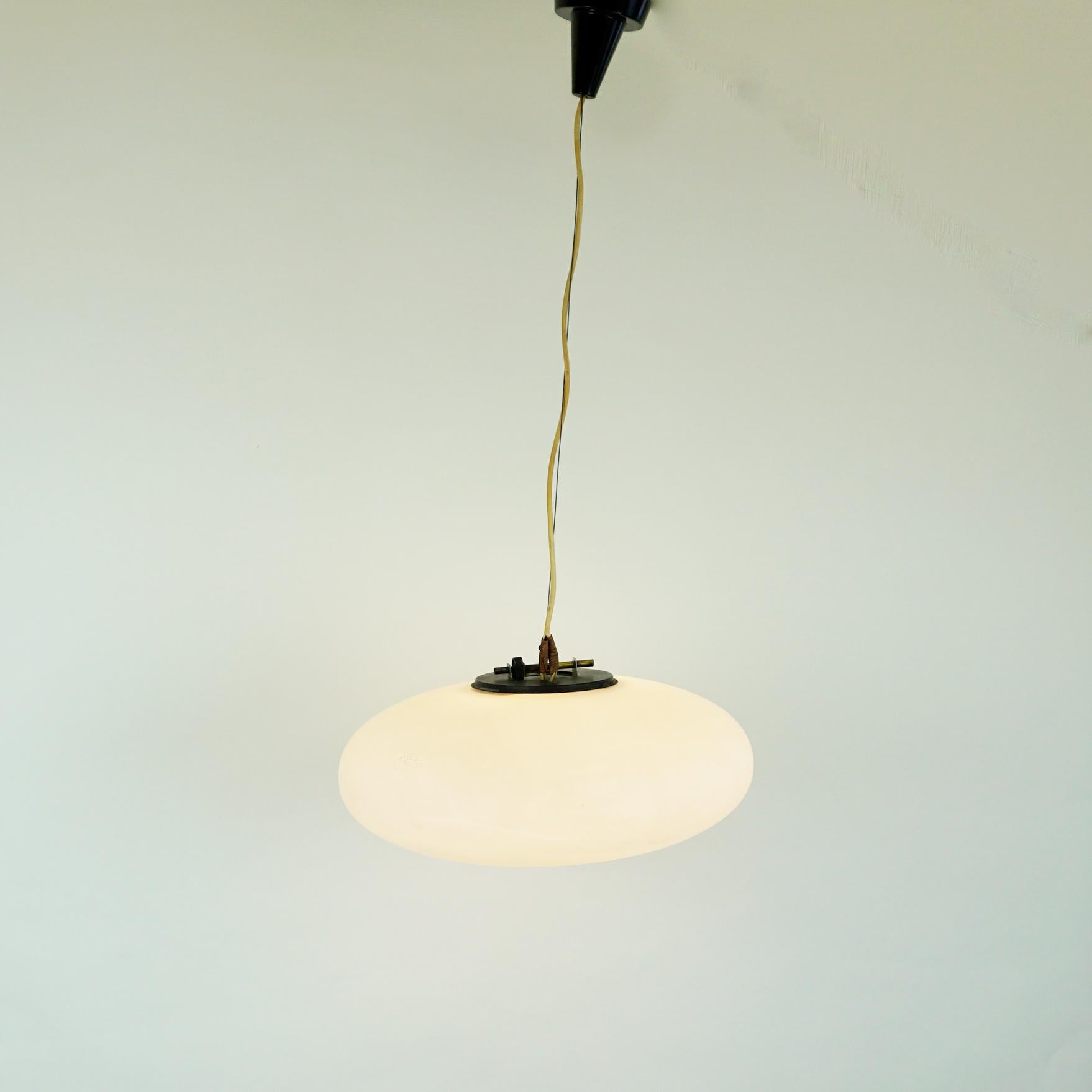 This charming midcentury pendant light was designed and manufactured in Italy and it´s shape is very close to lamps by Stilnovo. It features a beautiful oval opaline glass shade, black metal and brass details and a steel wire. The crème white