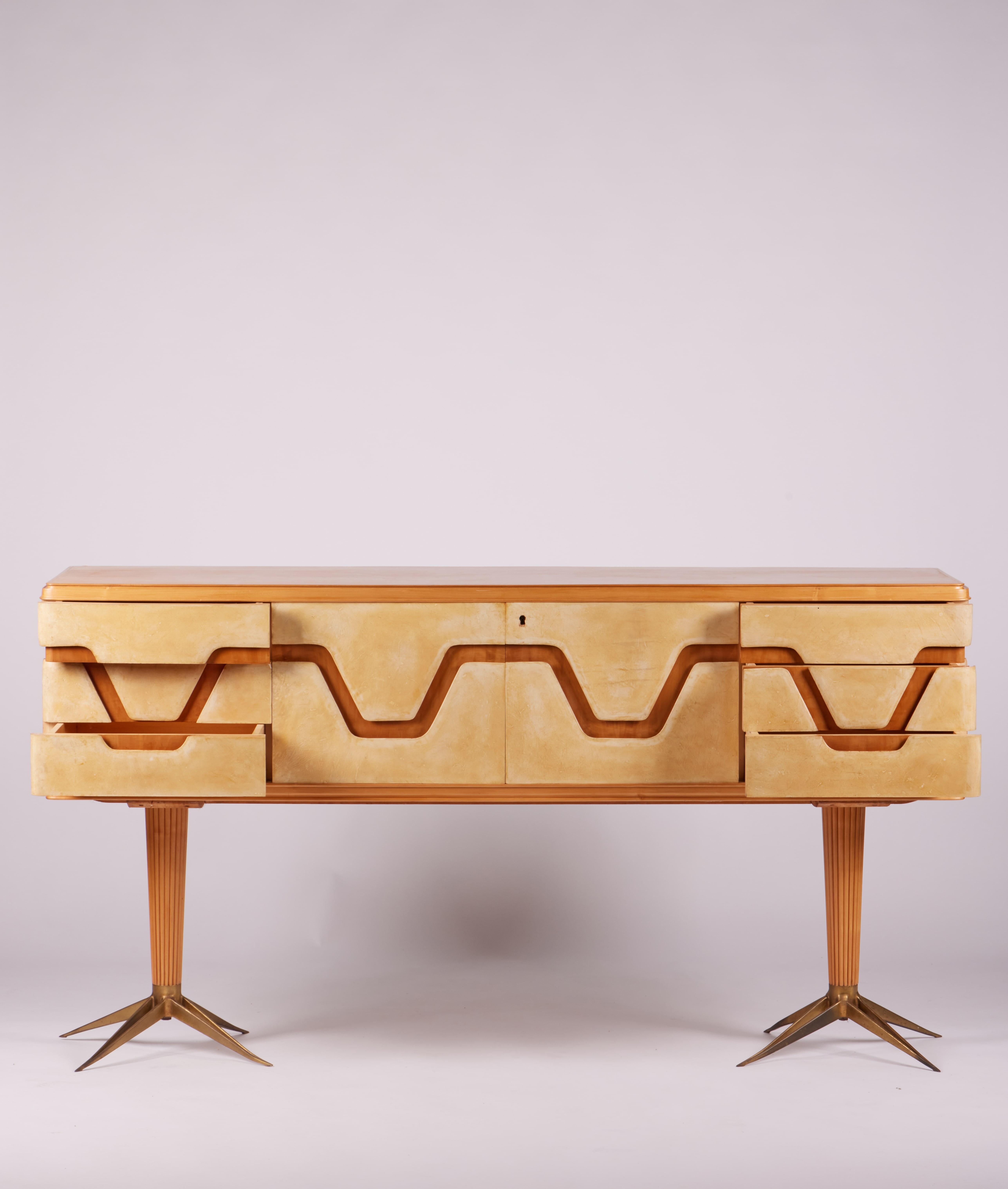 Italian midcentury parchment and walnut sideboard with brass and walnut legs, 1940s.

A well organized storing parchment and walnut main volume is held by two unique looking brass and ornate vertical wood elements.
Inside the sideboard, a