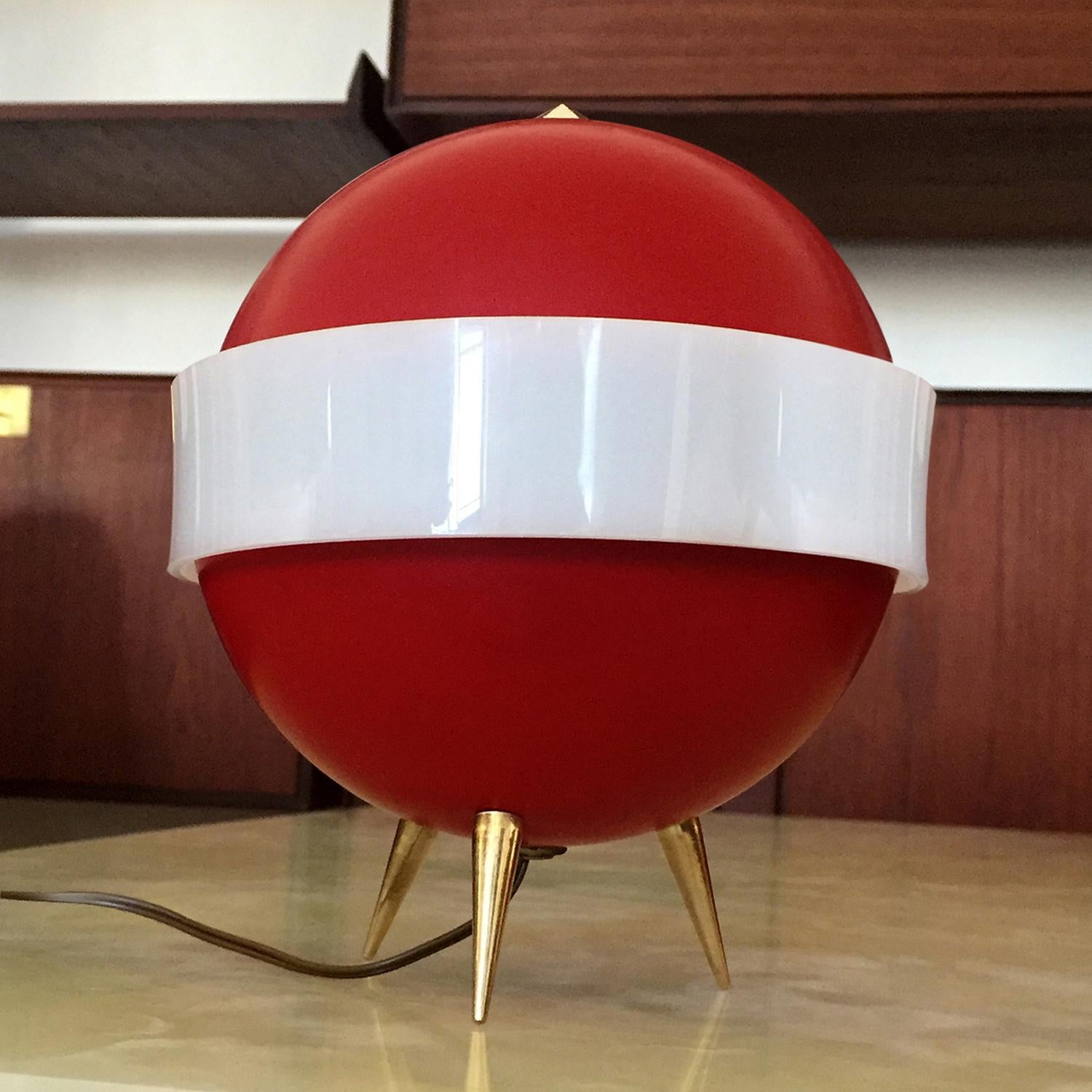 Very rare and unusual Italian table lamp designed by Angelo Brotto for Esperia in the 1950s, also named 'lumino’.
Its structure is composed by a metal sphere painted in red, supported by three brass feet, with around a white plexiglass band.
It's