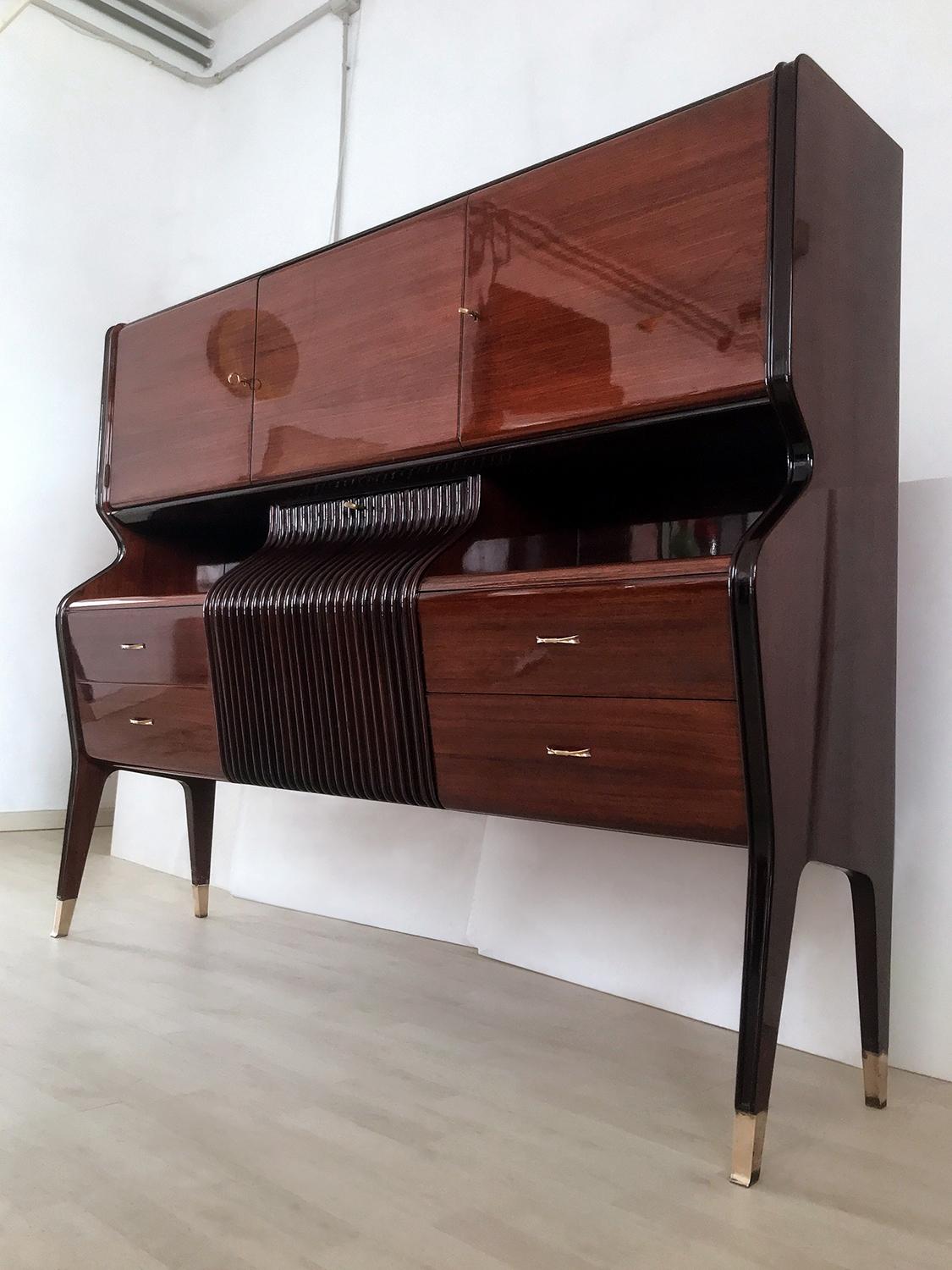 Stylish bar cabinet designed by Osvaldo Borsani in the 1950s.
Its structure is made of rosewood, characterized by a unique shape design given by its amazing curved frontal profile of the central drop-down door, very refined and finished with