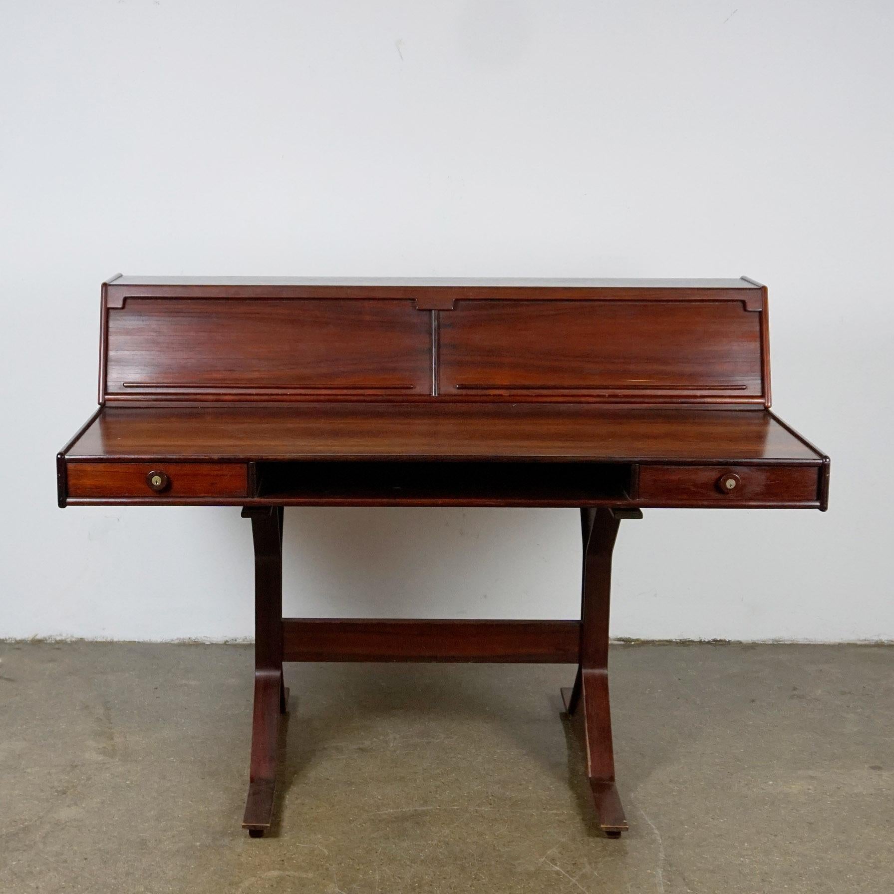 This excellent Italian Midcentury rosewood writing desk has been designed by Gianfranco Frattini for Bernini, Italy 1957, Modell No. 530.
It is made of beautifully grained rosewood and features a removable storage unit with tambour doors on top,