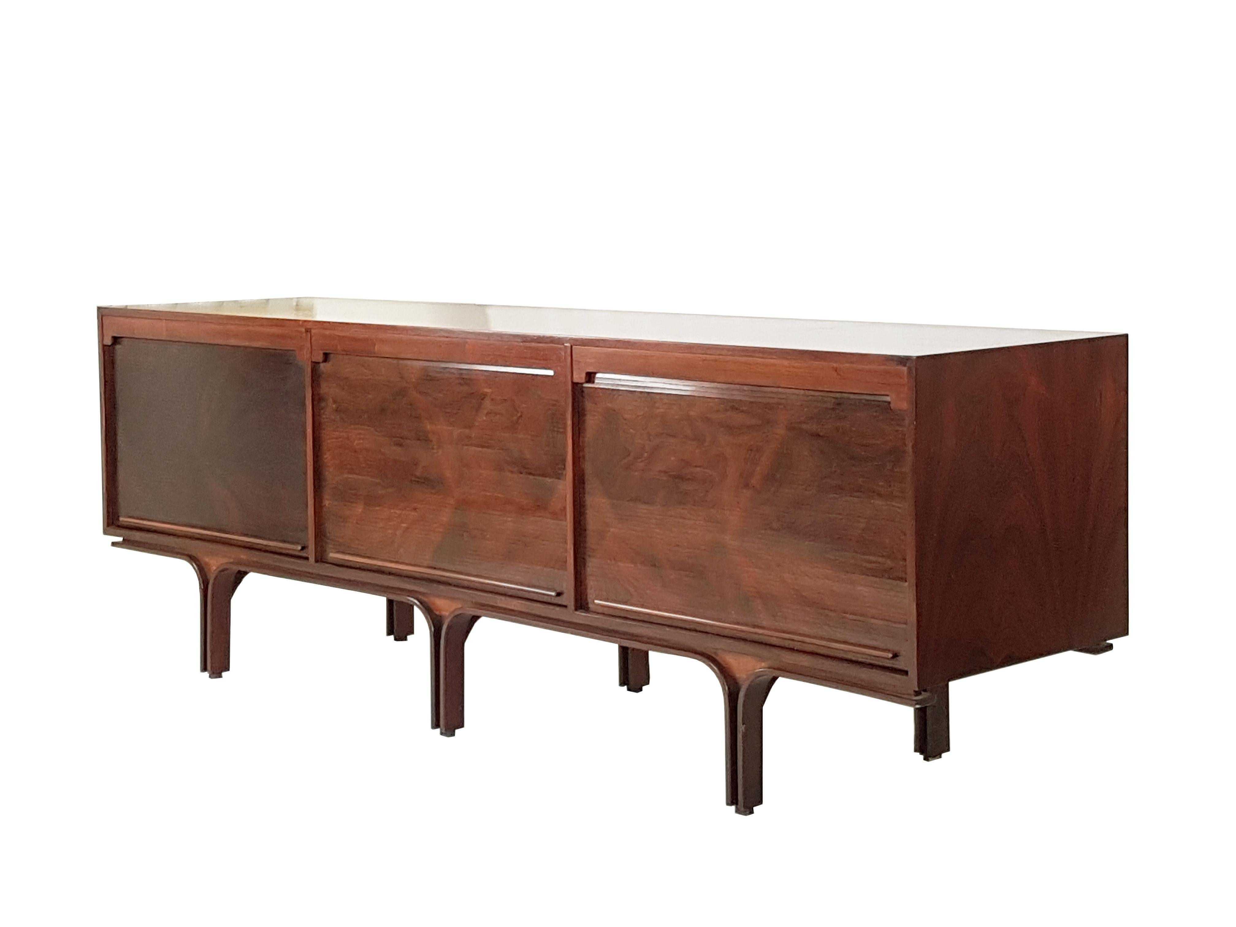 This Rio rosewood sideboard was designed by Gianfranco Frattini for Bernini in 1957. It is composed by 3 storage units with 2 shelves and 1 set of drawers. It features an useful vertical tambour doors system which allows you to hide the units and