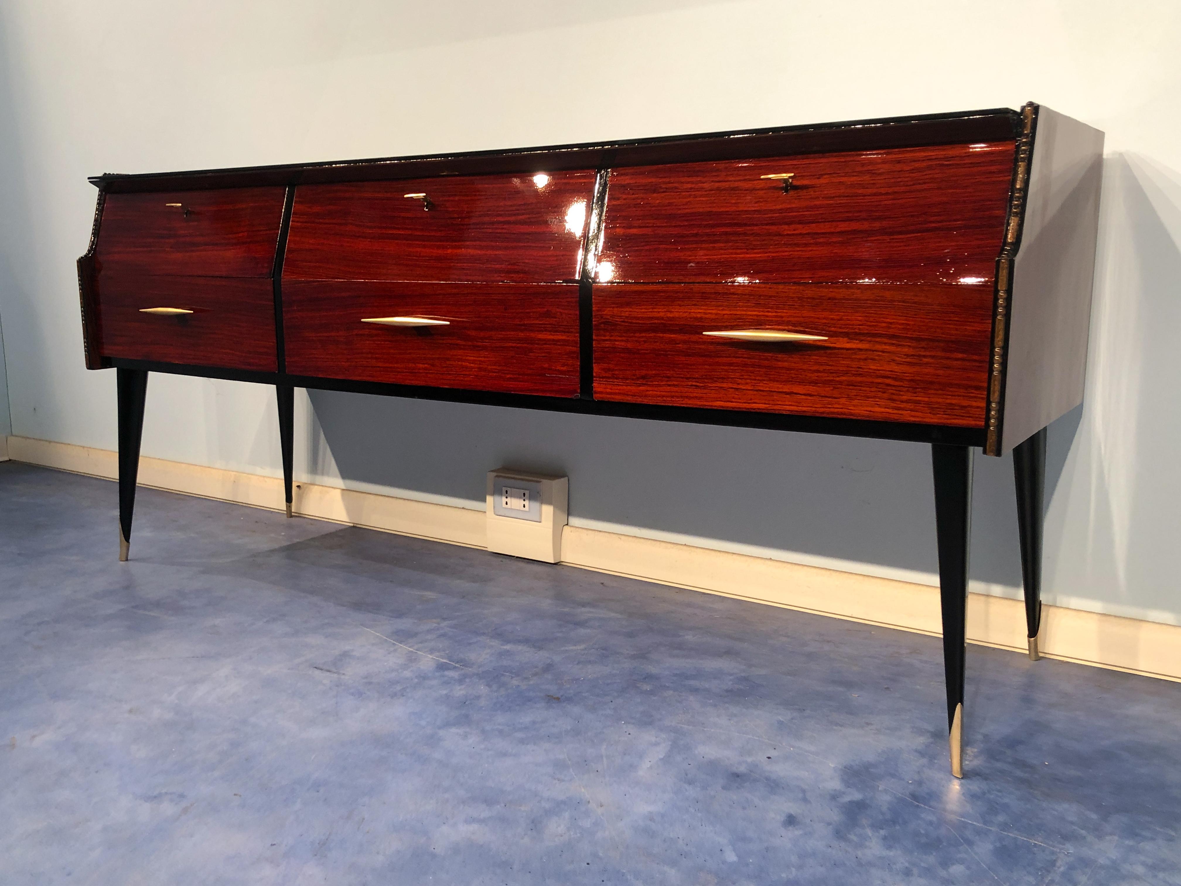 Beautiful Italian midcentury sideboard, or chest of drawers in refined teak with elegant details such as the brass handles and the arched line front. The top is in black glass, the interior of the six drawers are in maple, the legs finish in a