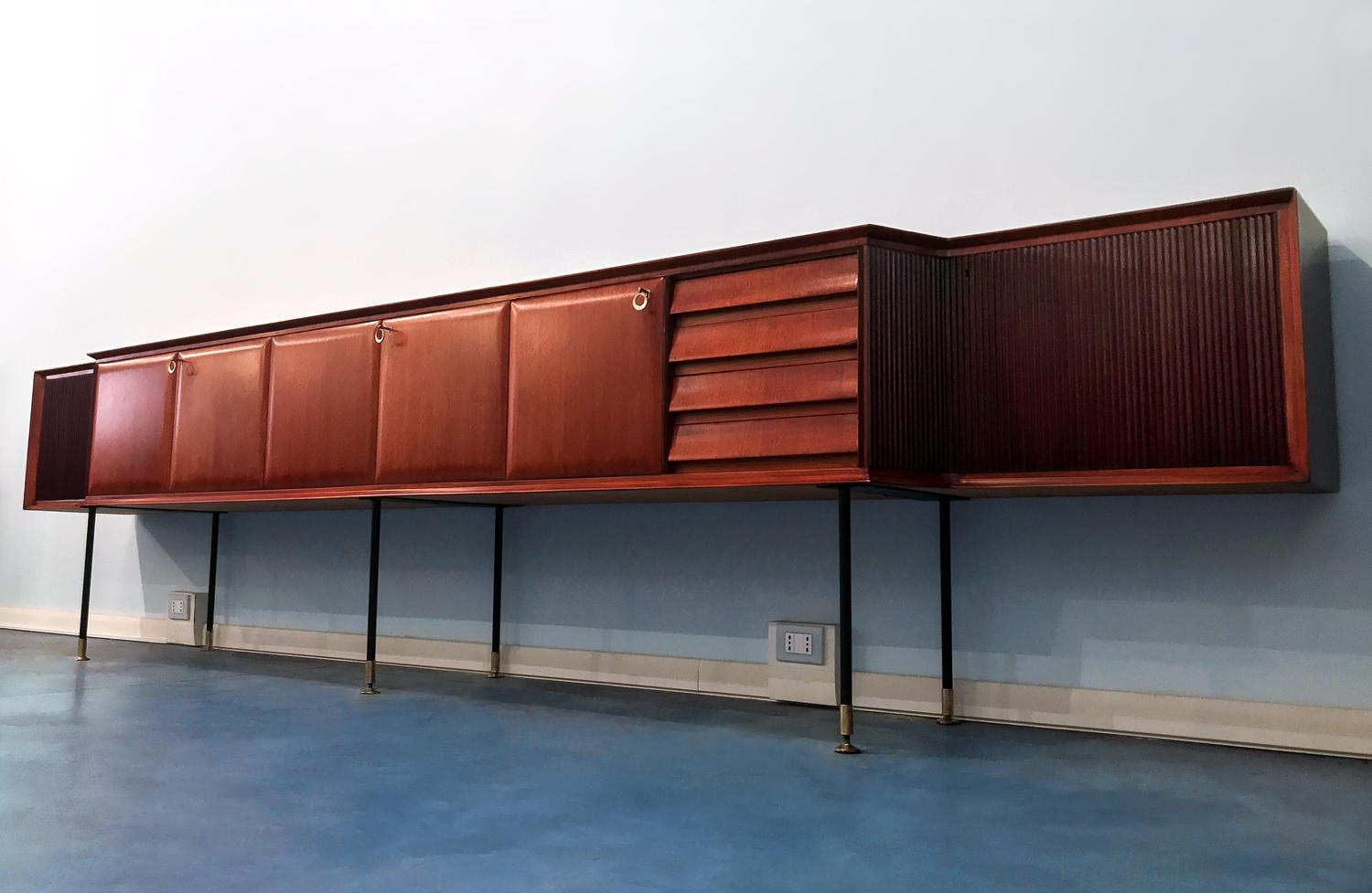 Stunning Italian teak wood long sideboard designed by Vittorio Dassi in the 1950s.
The structure is a unique piece composed by a long floating cabinet supported by metal legs finished with brass feet, and many cabinets with doors, partly in teak