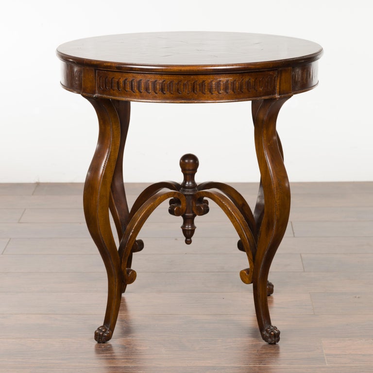An Italian vintage walnut round top side table from the mid-20th century, with cabriole legs, carved stretcher and inlaid apron. Created in Italy during the midcentury period, this walnut side table features a circular top with bookmarked veneer,