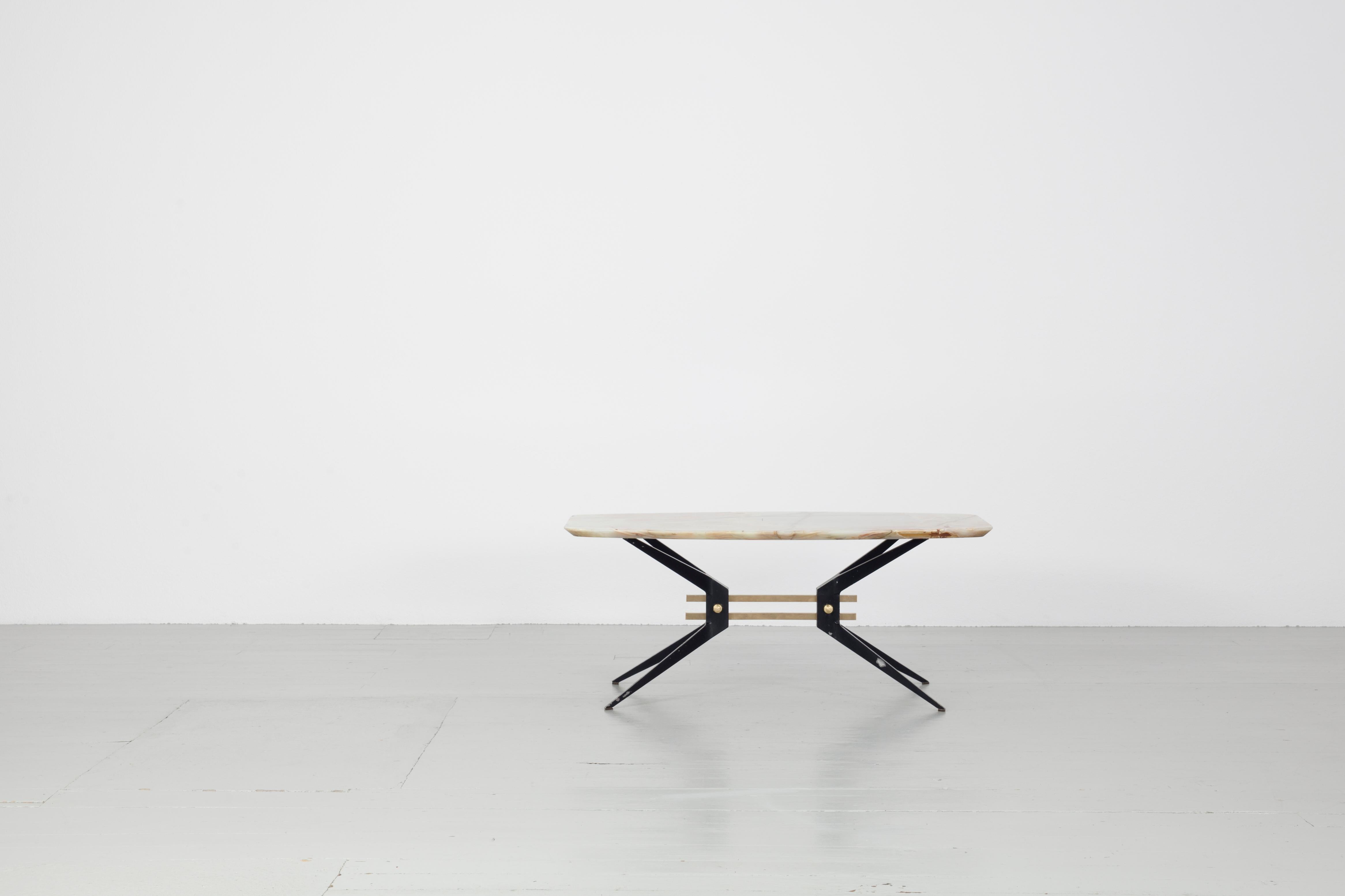Cette table basse robuste a été fabriquée en Italie dans les années 1960. Le cadre de la table, en aluminium laqué noir, constitue une base solide pour le lourd plateau en pierre. Deux entretoises en laiton relient les pieds effilés de la table pour