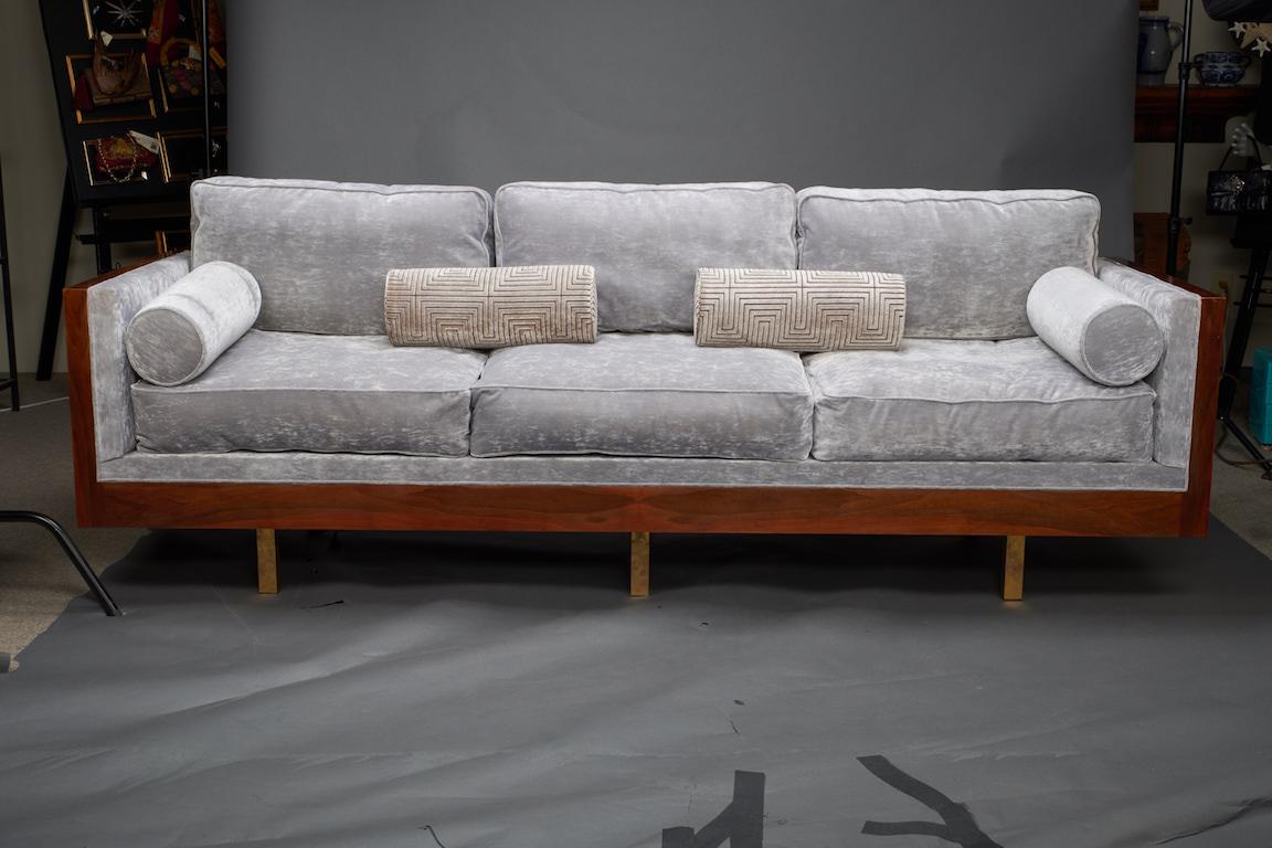 Sofa is re-upholstered in a grey velvety fabric. It has 3 big sit cushions and 3 pillows for the back support. 2 small cylindrical decorative pillows are also included. Frame of the sofa is made out of walnut wood. It is elevated by 4 small legs on