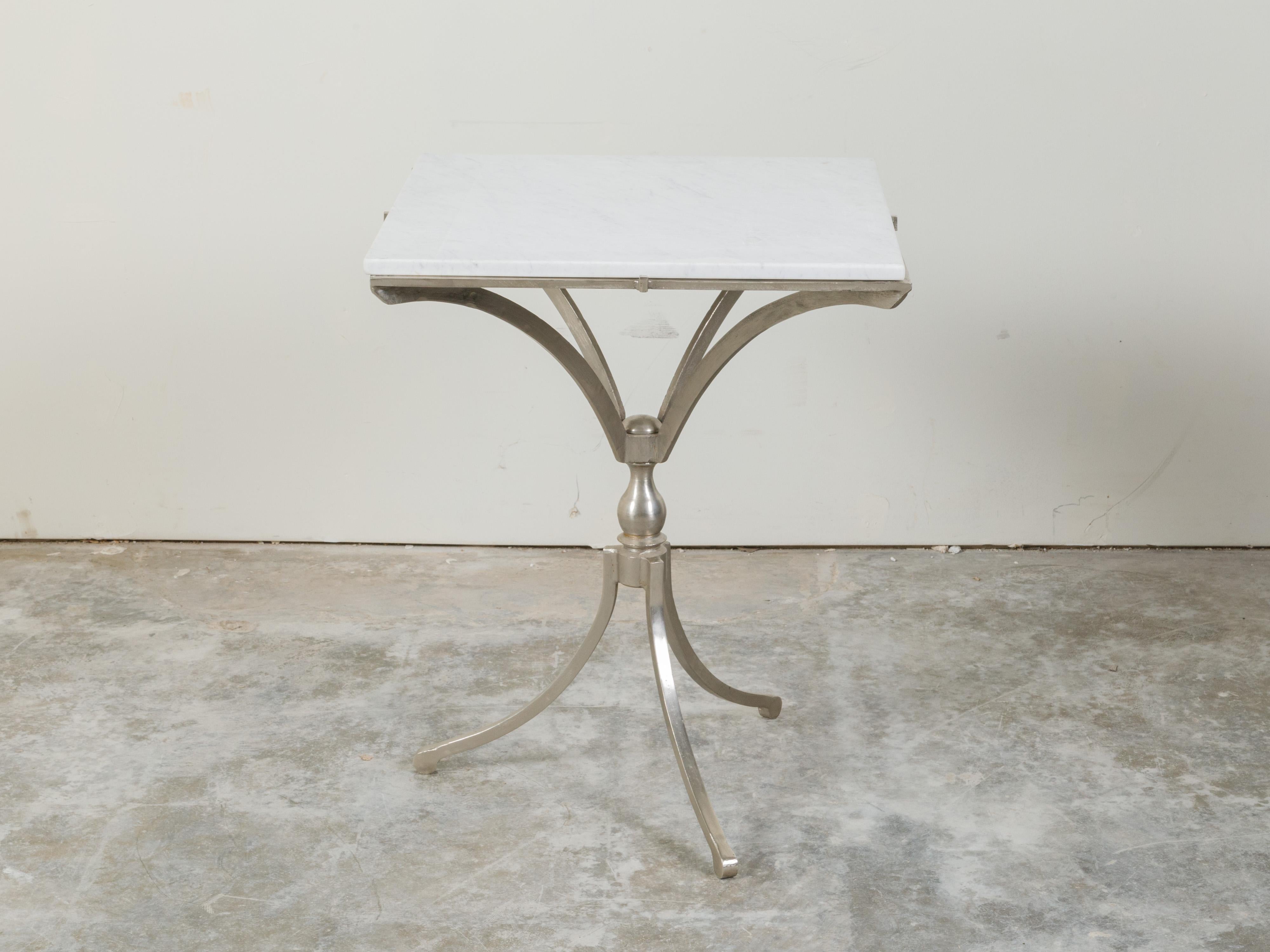 An Italian steel table from the mid 20th century, with white marble top and tripod base. Created in Italy during the midcentury period, this steel table features a square-shaped white marble top sitting above a steel structure with tripod base.