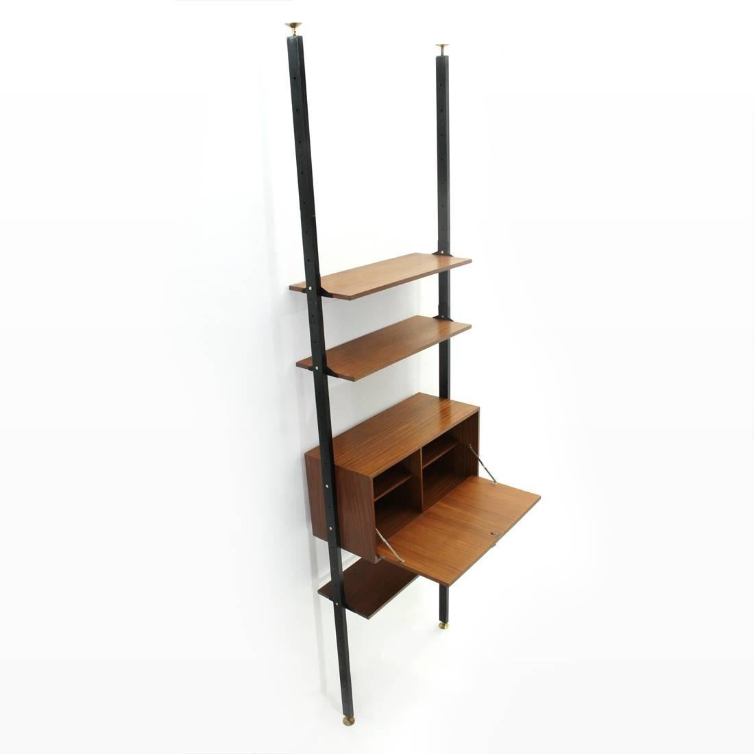 Italian manufacture wall unit from the 1950s.
Uprights in black painted metal with adjustable brass feet.
Shelves and containers, in teak veneered wood.
Container compartment with internal shelves and folding door.
Brass handle and