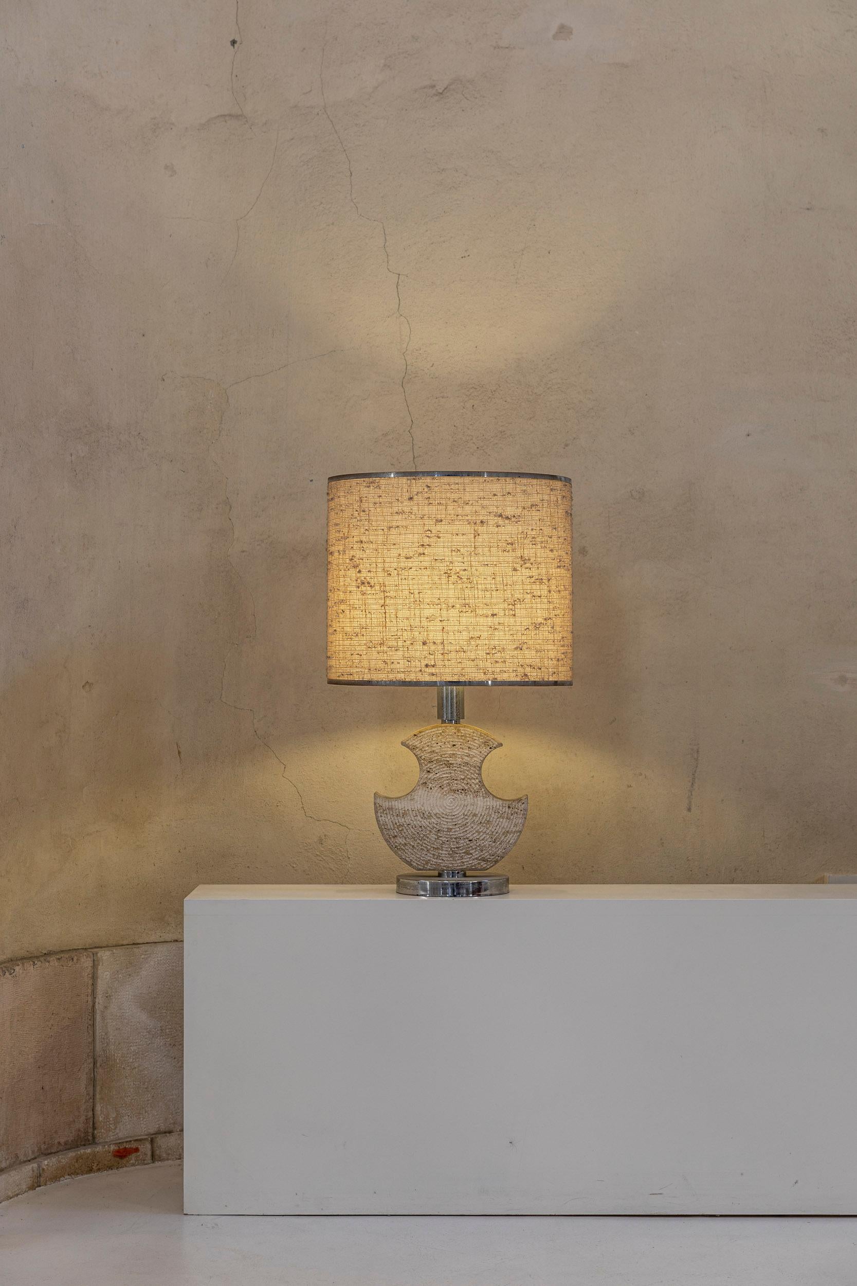 Midcentury Italian table lamp with a stunning base made of carved travertine and chrome, original fabric lampshade, perfect condition. 
Measures: Height: 80 cm 
Diameter shade 47 cm
Diameter base 21,5 cm
Width of the sculpture: 30 cm.


