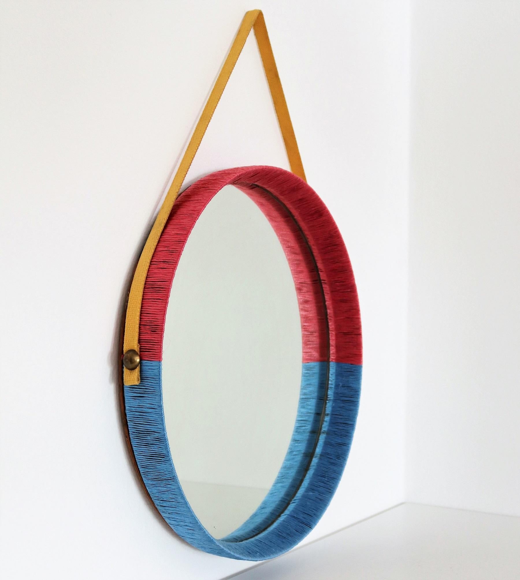 Beautiful und unique Italian mid-century wall mirror with yellow hanging ribbon.
Made in Italy in the 1950s.
The mirror is most probably inside made of chestnut and have been covered by an artisan with a red and blue cord and hung on a wall hook