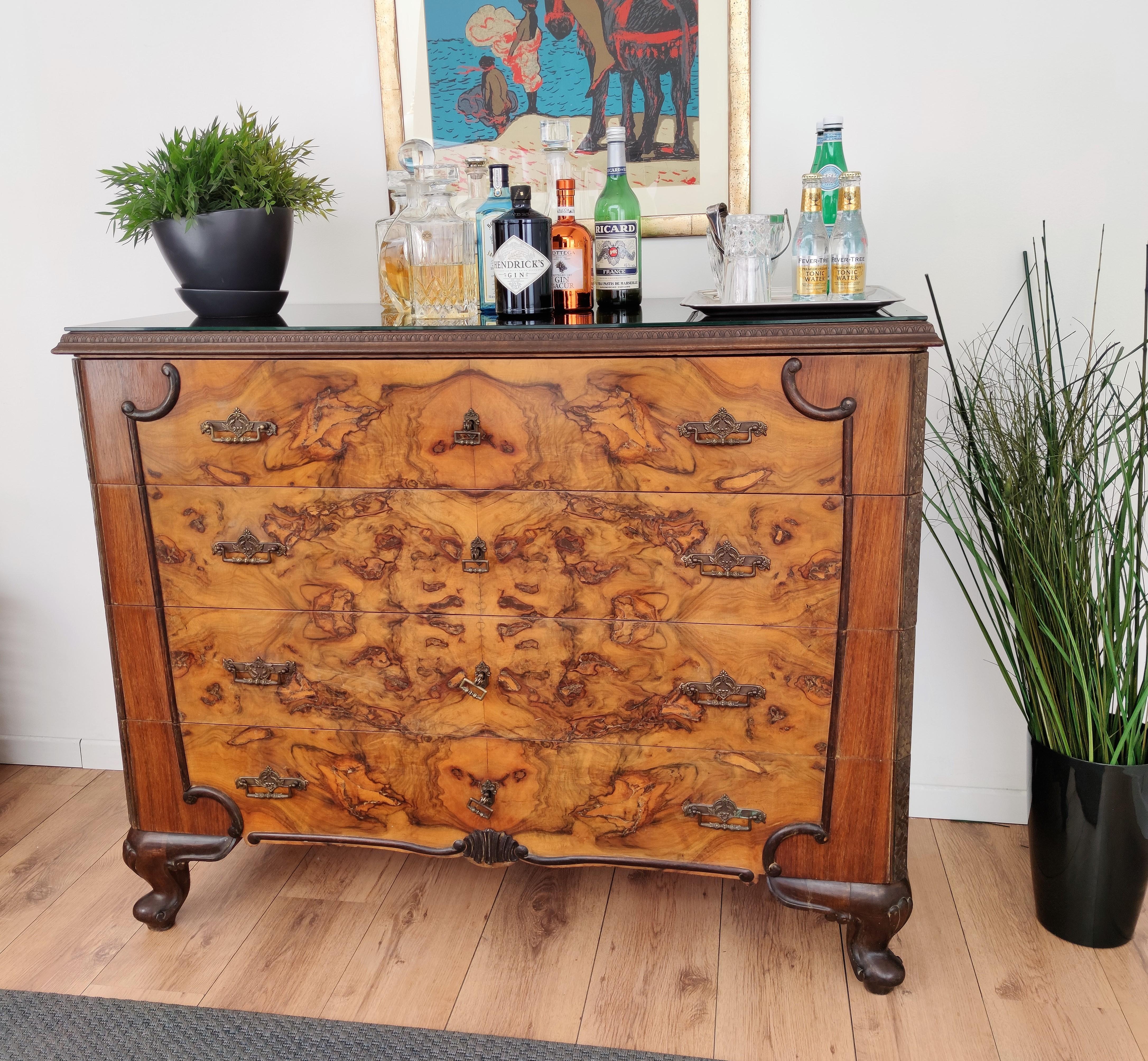 Very elegant walnut burl Italian Art Deco Mid-Century Modern chest of drawers, commode cabinet with 4 drawers and brass decorated handles and keys with black glass top. The unique and typical design and shapes make this a true statement piece in any