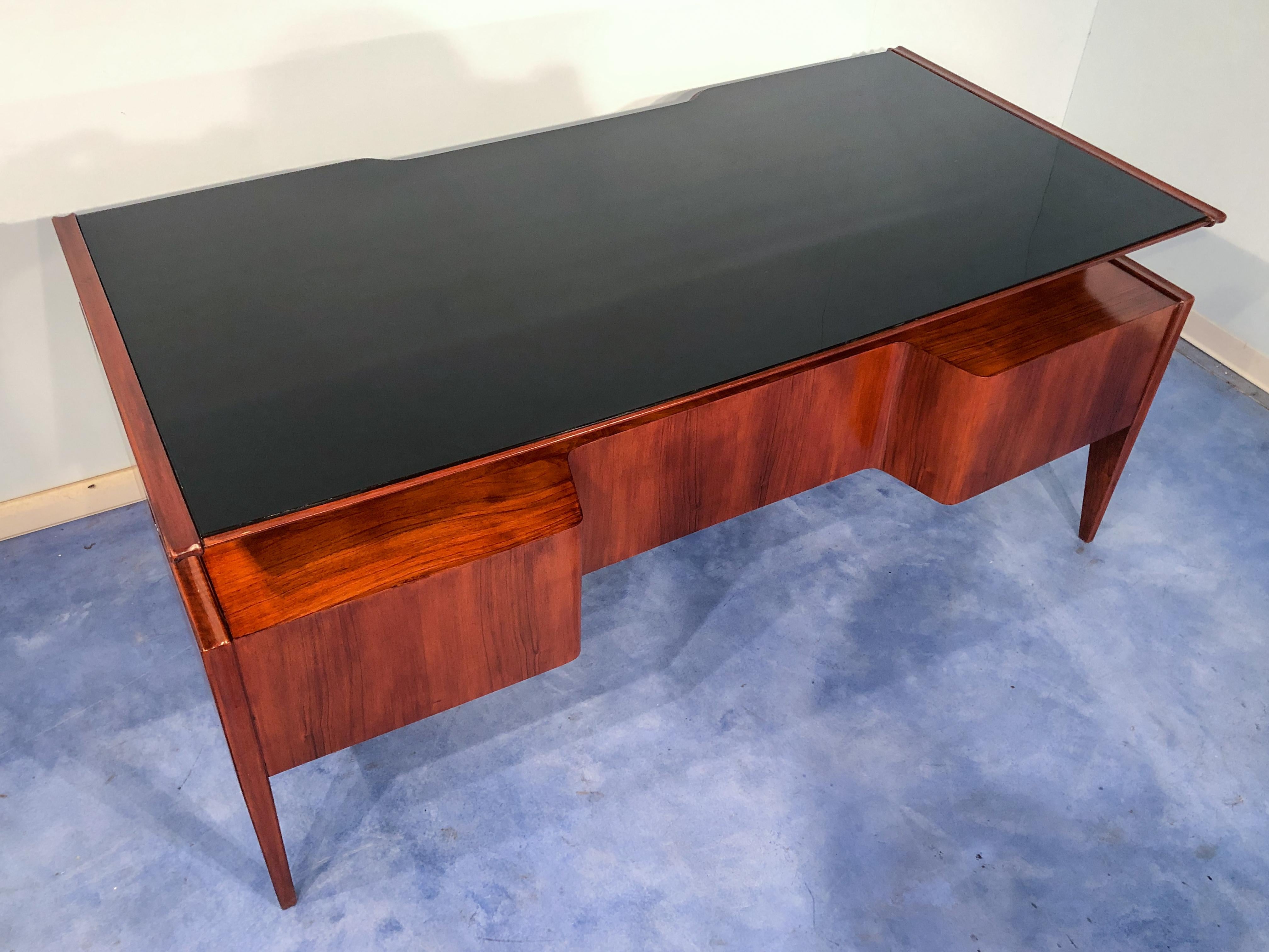 Outstanding Italian midcentury executive walnut desk. Very well designed and attributable to Guglielmo Ulrich in the 1950s.
The top has a curved shape and the surface in black glass, the contrast between the walnut gives elegance and sophistication