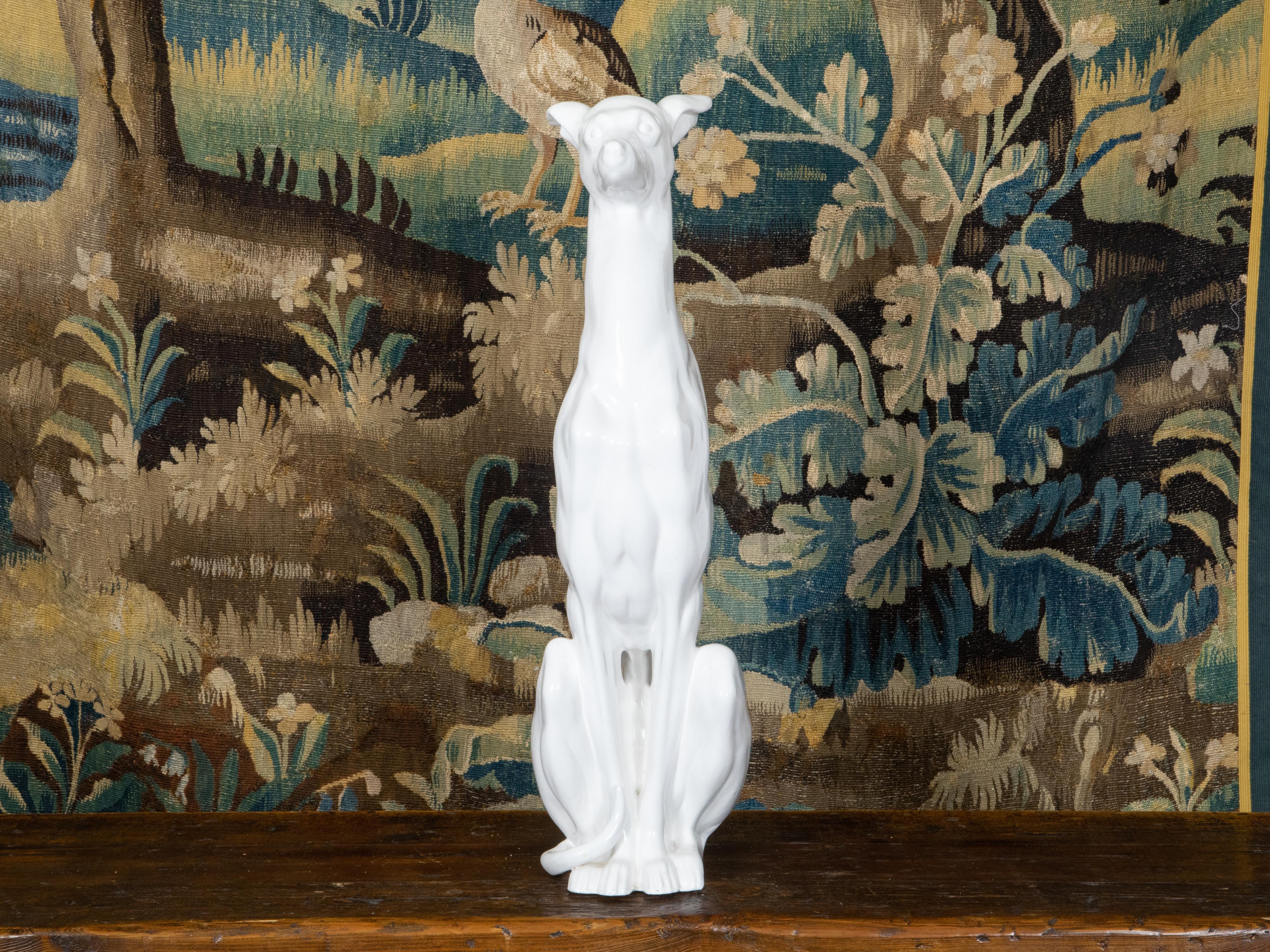 A vintage Italian white porcelain dog sculpture from the Mid-20th Century depicting a greyhound obediently sitting on his hind legs. Created in Italy during the Midcentury period, this porcelain sculpture draws our attention with its handsome