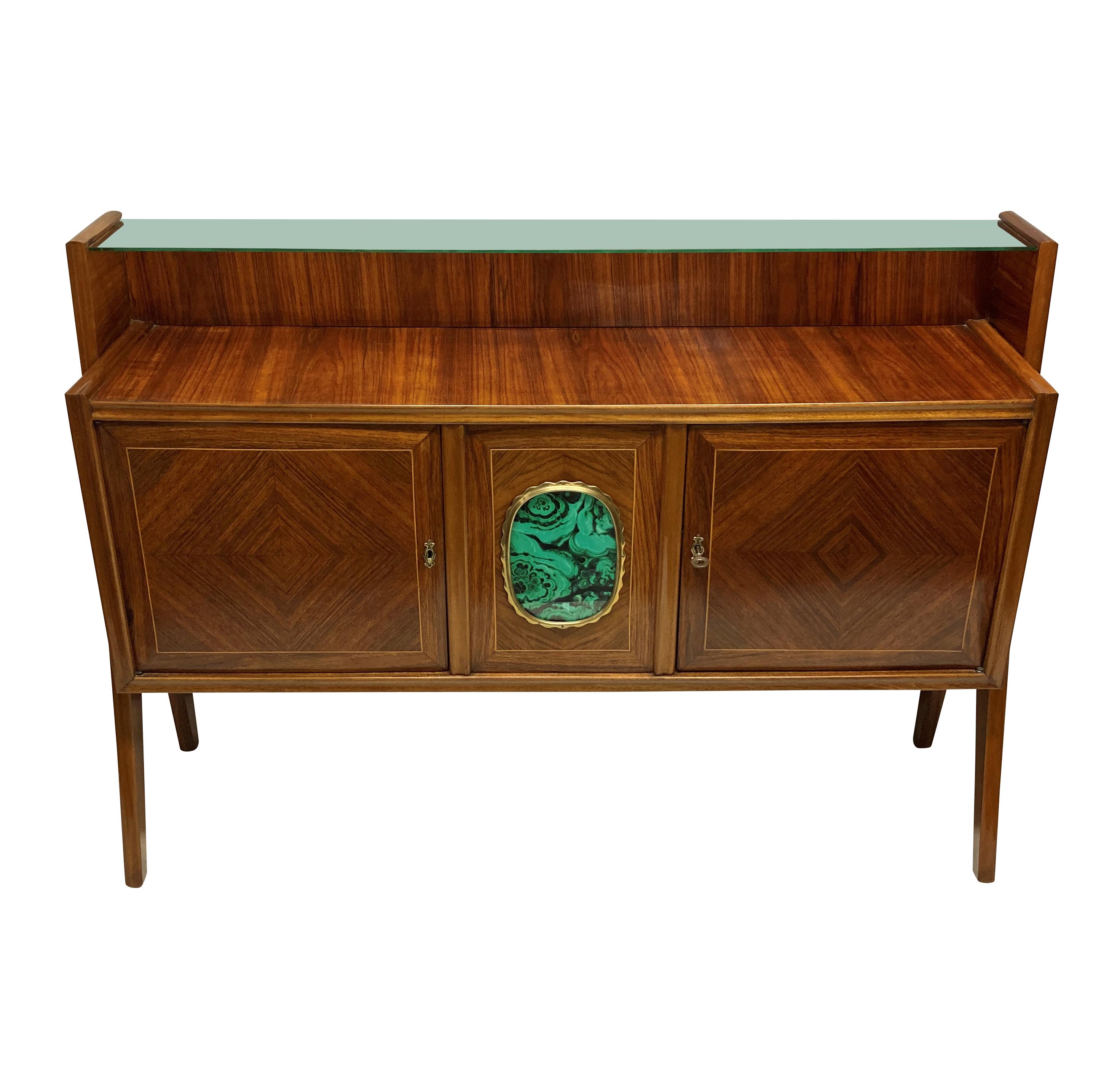 A stylish Italian mid century credenza, beautifully veneered in zebra wood, with a central two door cupboard & upper glass shelf. The central panel with brass detailing and a faux malachite panel, supported each side with architectural legs.