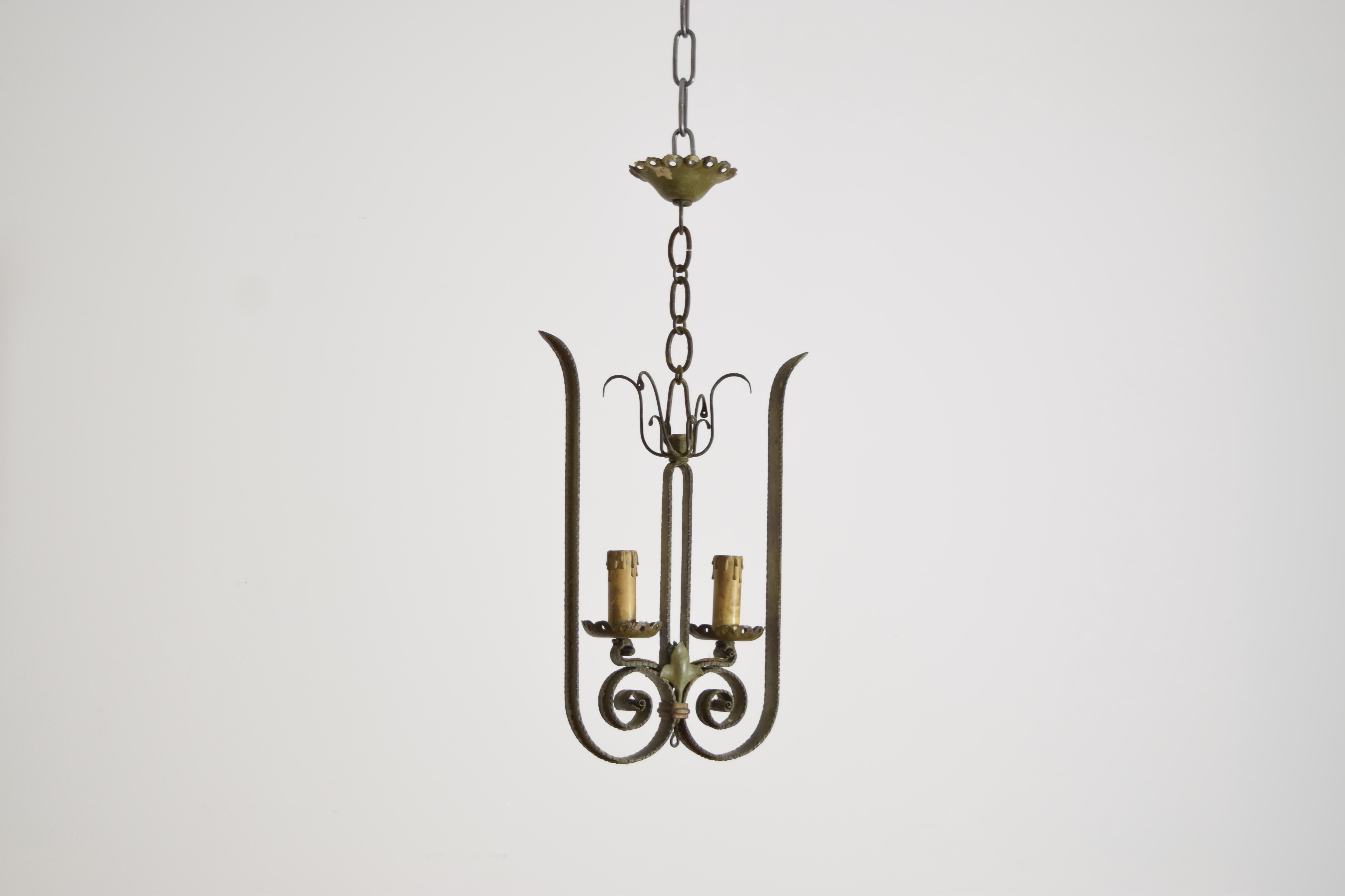 two large scrolls join to form the body of this chandelier, with pierced bobeches atop the lower parts of the scrolls, the green paint now faded and characteristic of iron work from Milan in the early 20th century