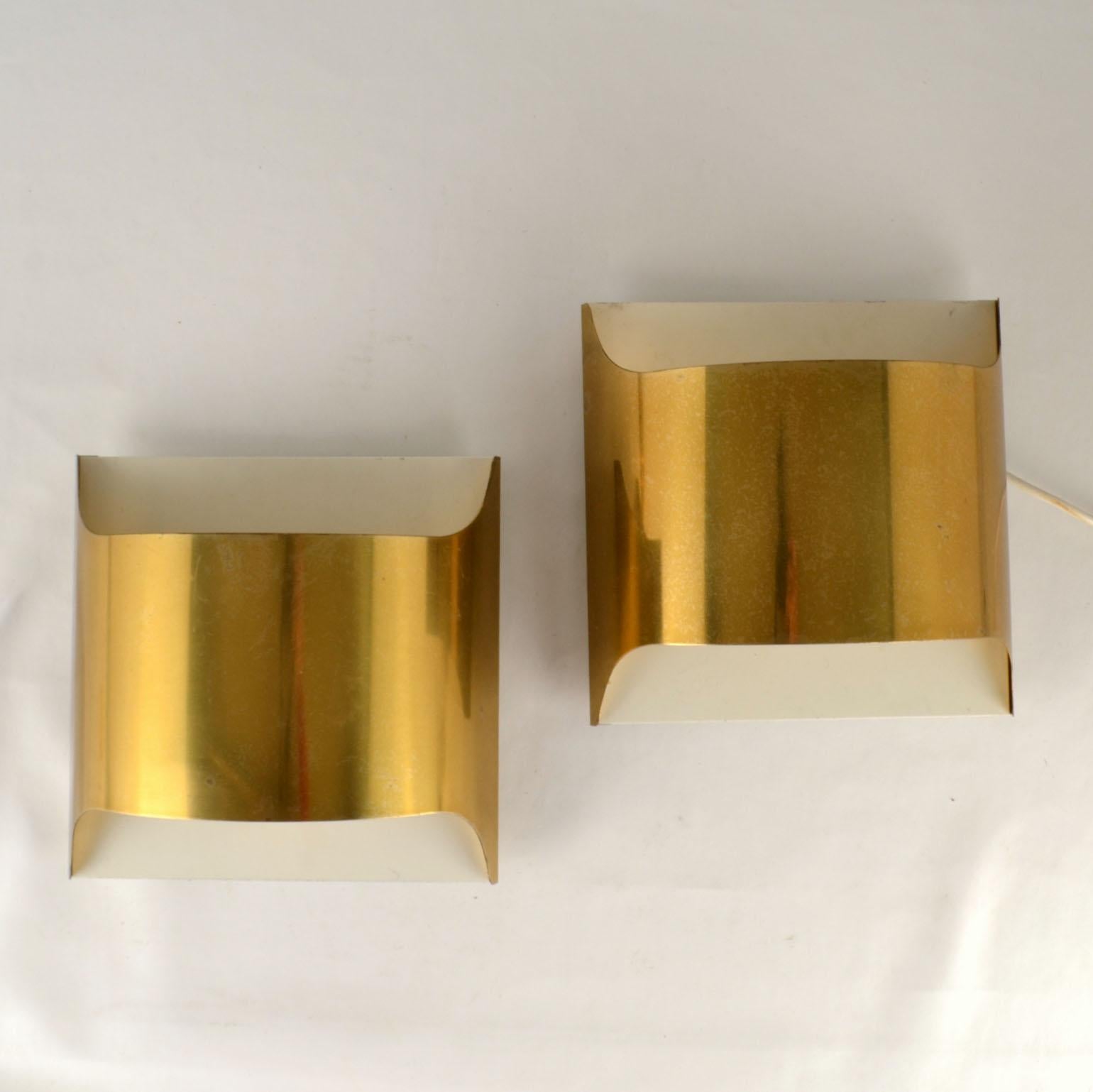 Pair of Italian minimalist brass 1960's wall mounted sconces are made of curved sheet encased in a flush mount metal wall bracket. The wall lights are creating up and down wall washed light that is reinforced by Internally white enamel reflection.