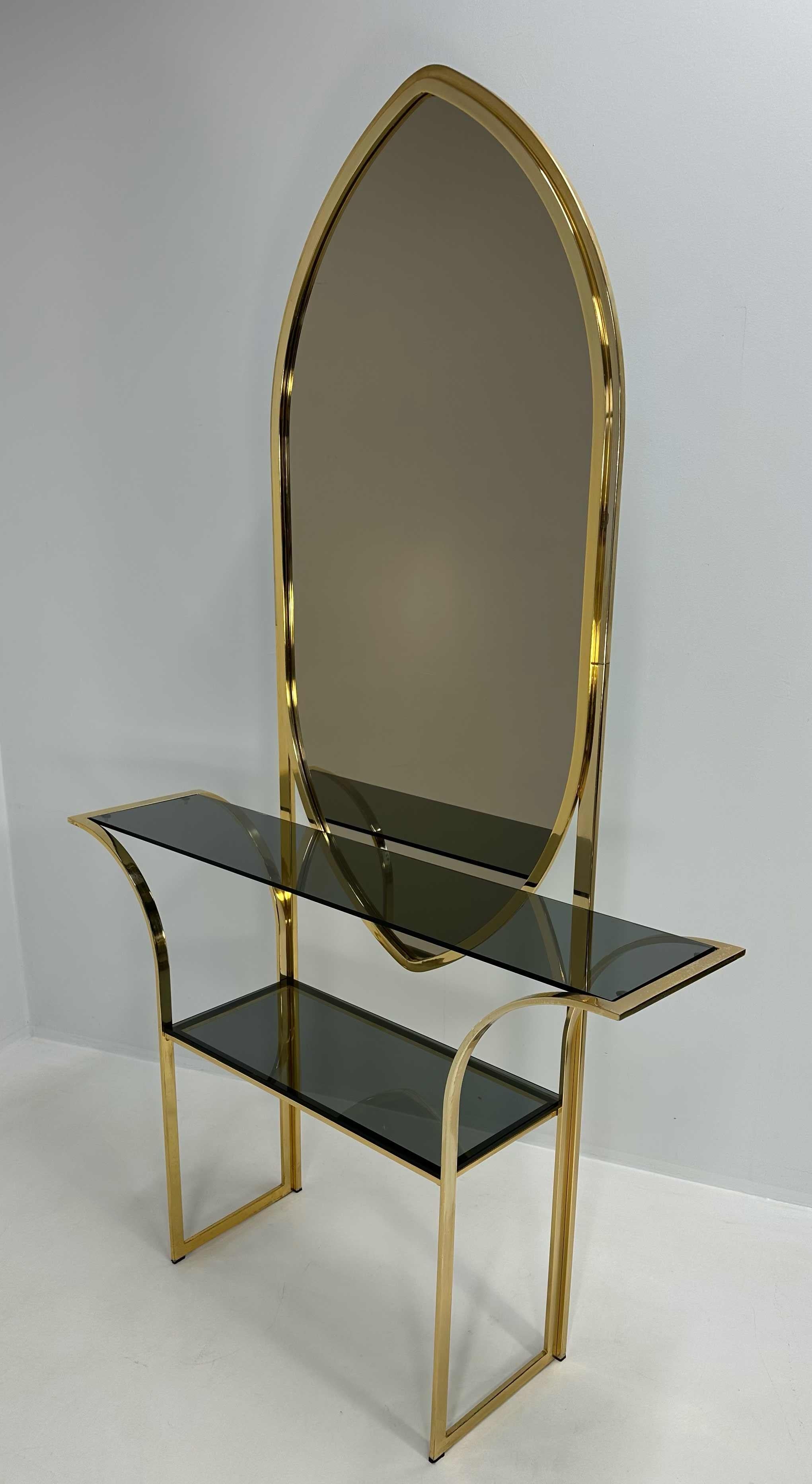 Italienische Konsole aus den 1970er Jahren aus Messing mit Ablagen aus Rauchglas und einem passenden Spiegel. Die Struktur zeichnet sich durch geschwungene Linien und geschwungene Beine aus, die zwei dunkle Glasböden tragen. Der hohe, spitz