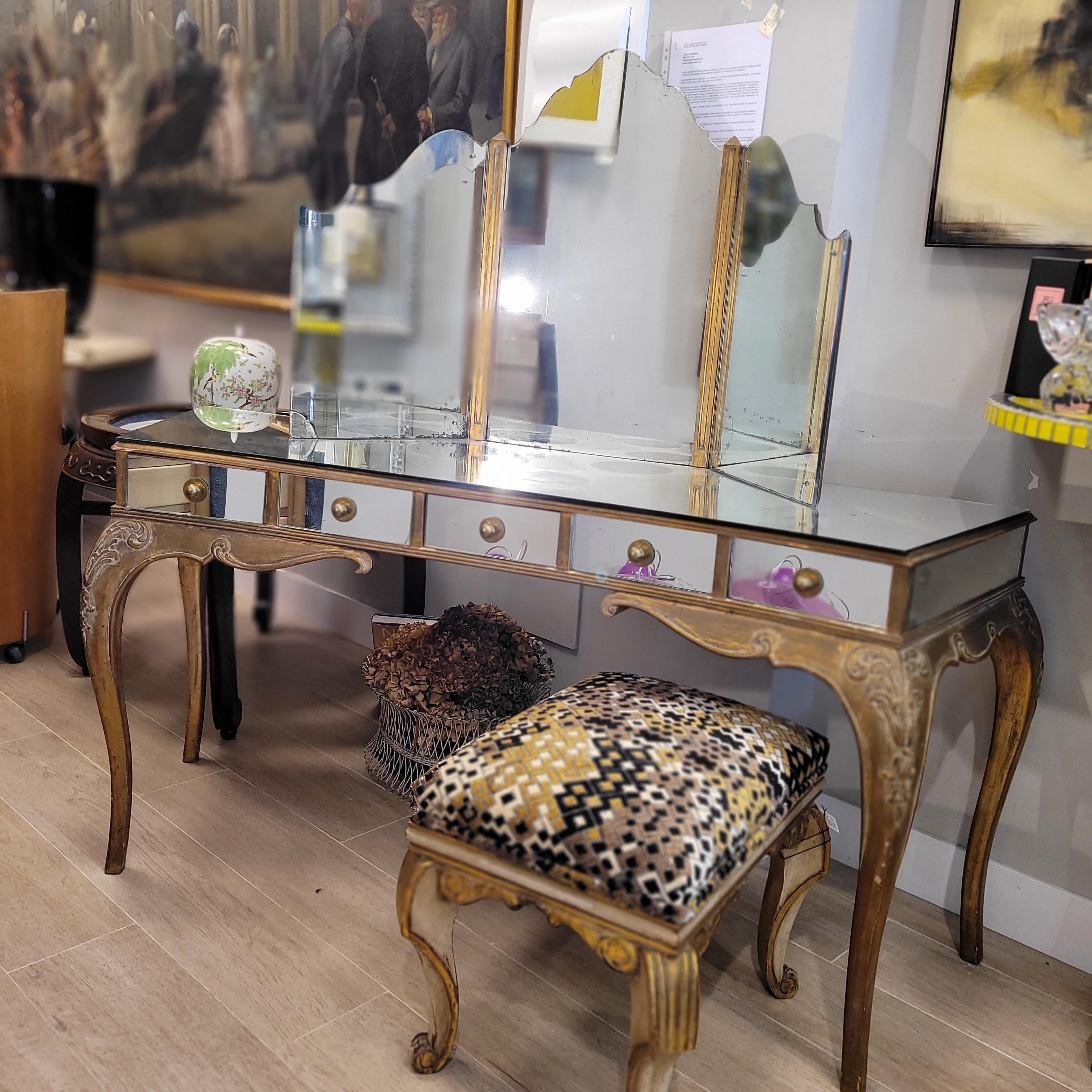 Unique Italian mirrored vanity, Hollywood Regency style and period, 1970s.
The central body has a slightly curved profile resting on four carved and gilded wooden legs, decorated with delicate inverted chain scrolls.
The skirt follows the same