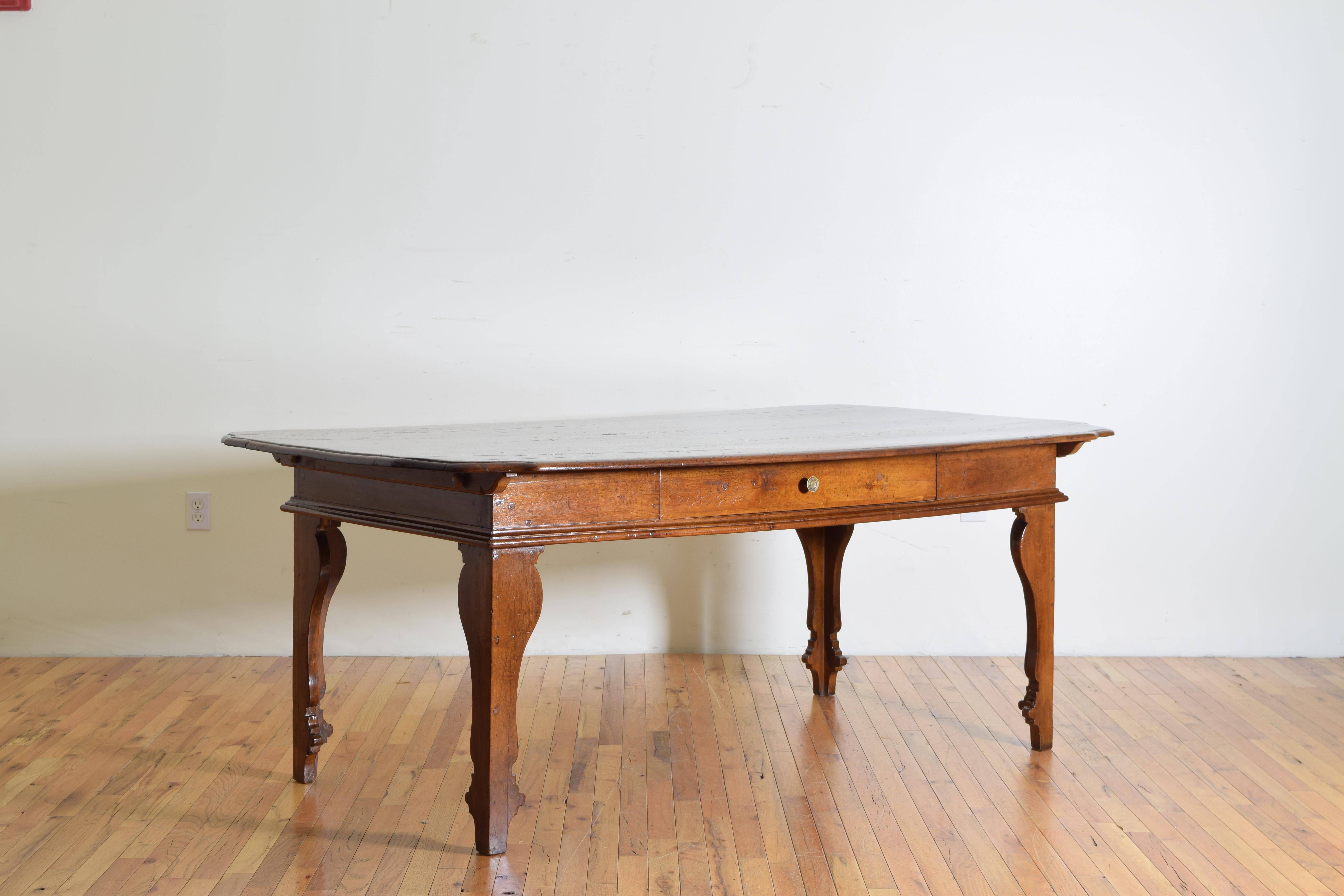 Likely used as a kitchen or library table, having a rectangular top with bow shaped corners and various inlaid patches, the apron housing one drawer accessible on both sides, raised on uniquely shaped and tapering legs.