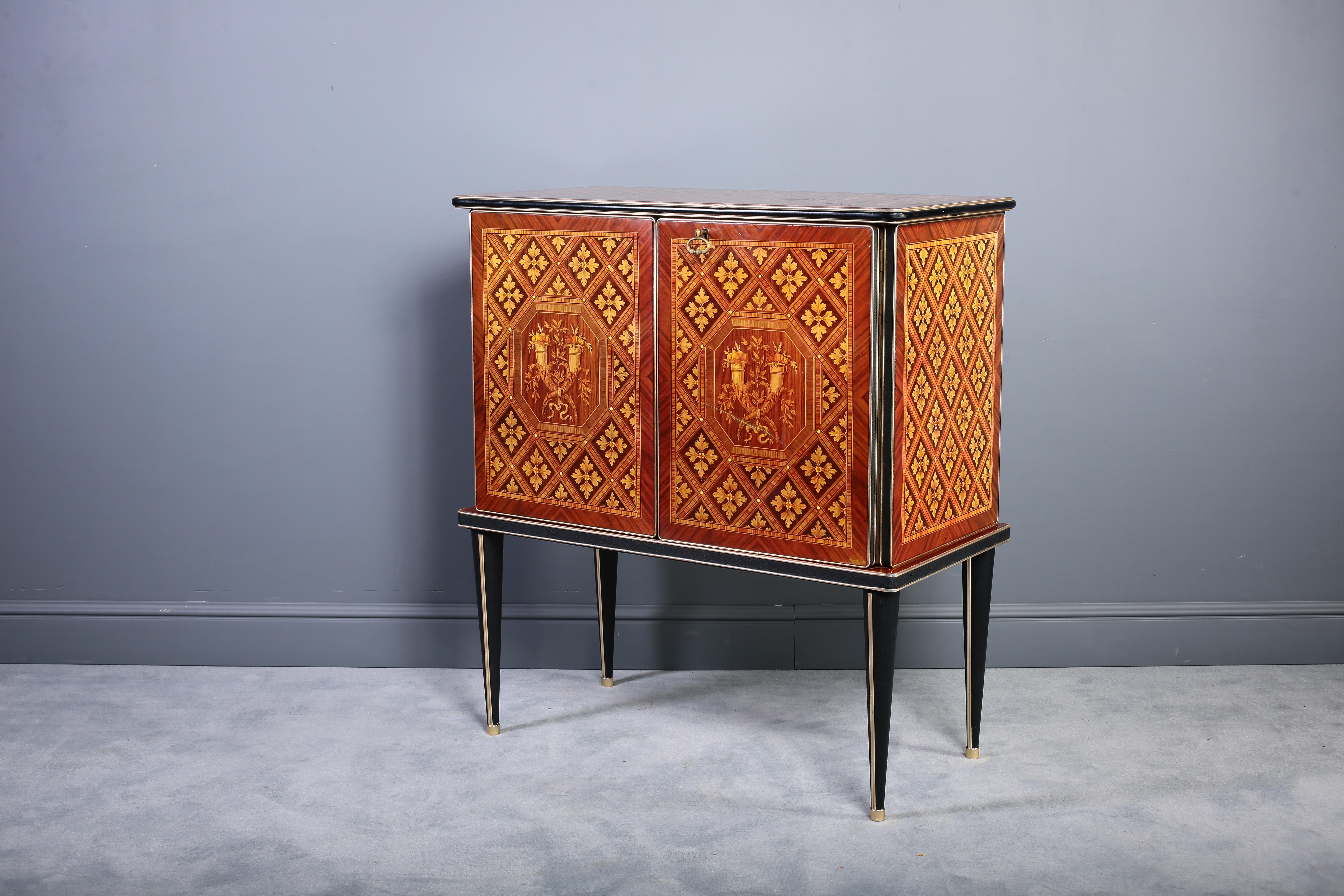 This early 1950s bar cabinet was created by Umberto Mascagni of Bologna, in Italy, and imported to the UK by I. Barget and retailed through Harrod's, London, between 1952-1955. It has tapered legs and is finished with brass feet. The back of the