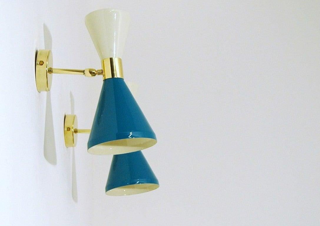 The wall sconce or reading light shown in un-lacquered natural brass with white and blue enamel fabricated in Italy by Fabio Ltd. 

The cones are a vintage 1950s Italian design. The wide band and distinctly beveled edge make a strong design