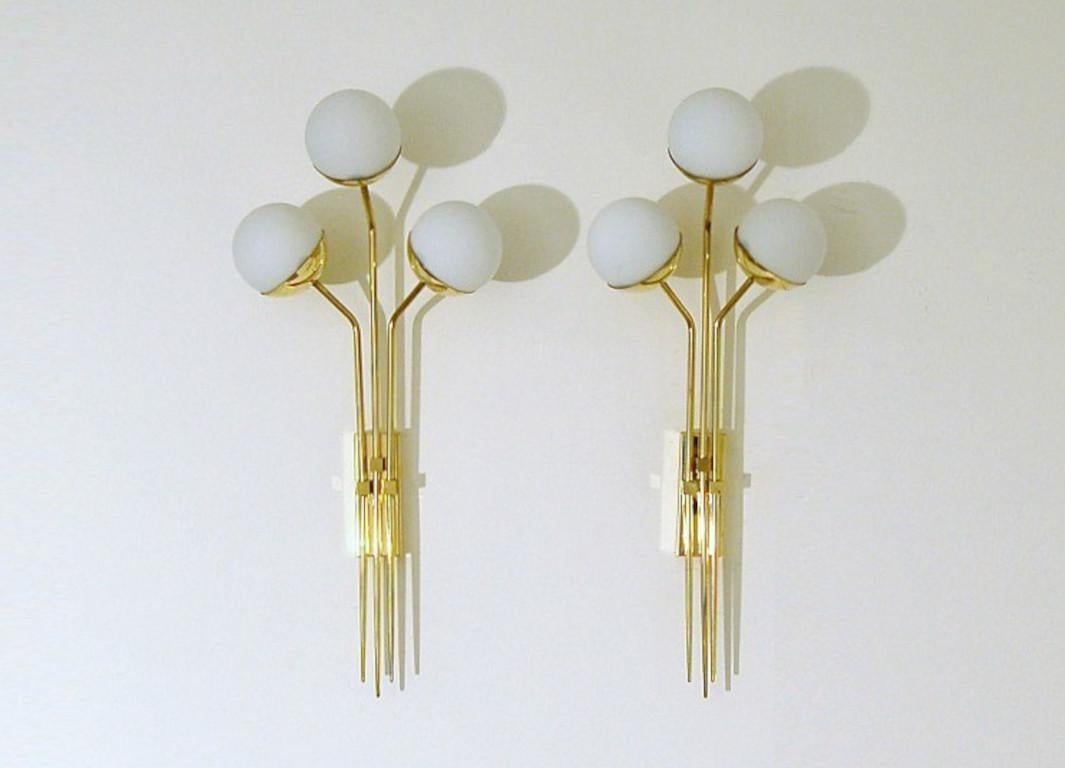 Elegante aplique de pared de latón natural sin lacar con globos de cristal opalino lechoso fabricado en Italia por Fabio Ltd. 

Se trata de una interpretación moderna y contemporánea de un aplique clásico, muy influida por el Modernismo italiano de