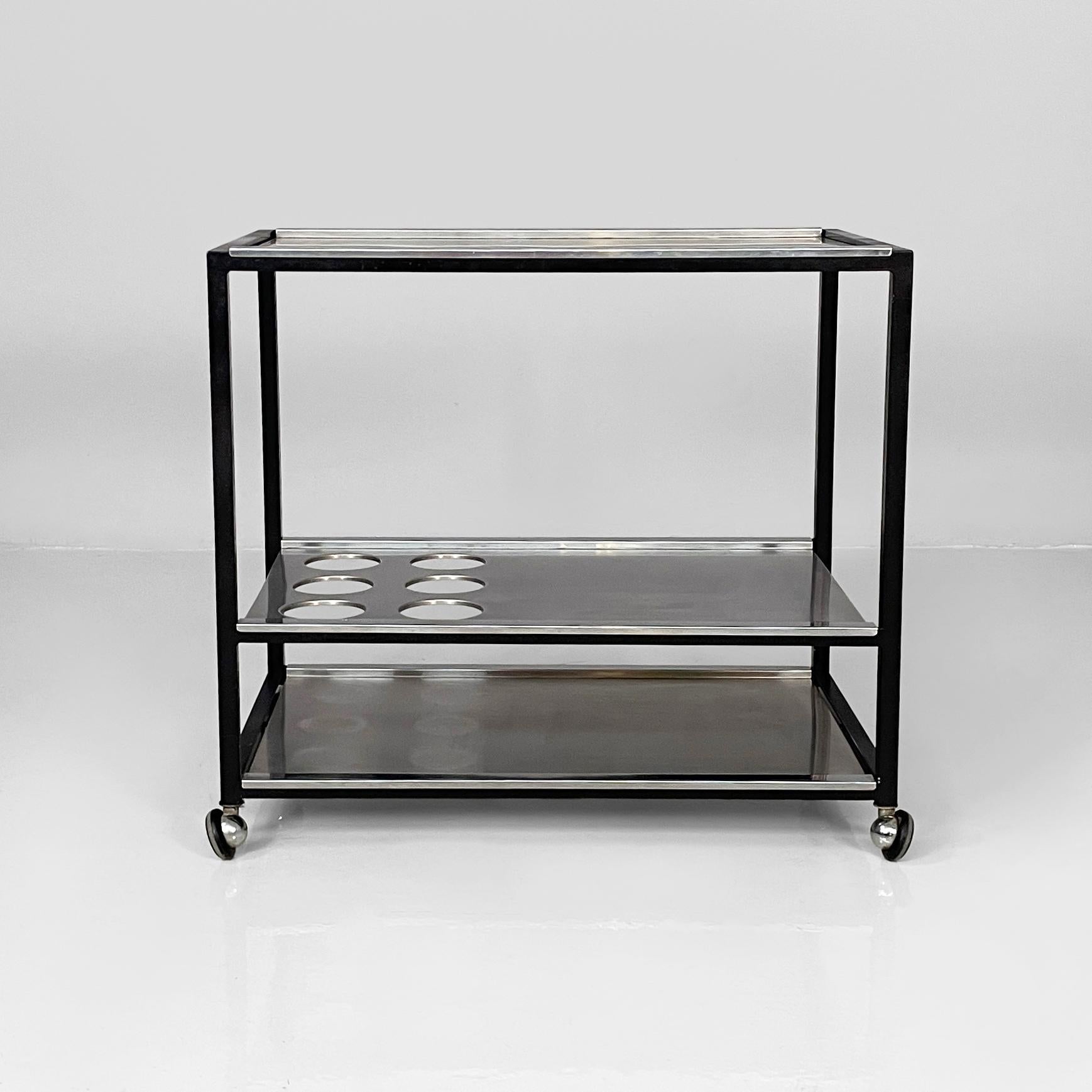 Carrello moderno italiano con portabottiglie in acciaio e metallo nero, anni '80
Carrello con tre piani rettangolari in acciaio. Il secondo ripiano è dotato di sei portabottiglie. Il telaio a sezione quadrata è realizzato in metallo verniciato nero.
