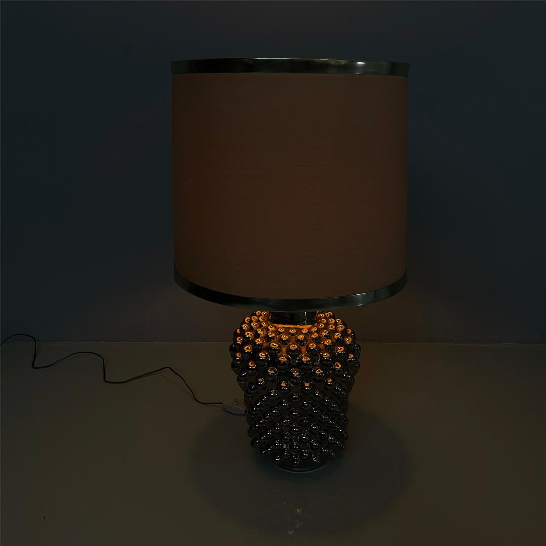 Italian modern ceramic table lamp by La Farnesiana, 1970s
Round base ceramic table lamp. The lampshade is in beige fabric with two metal bands.
The base, narrower at the base and widening towards the top, is in silver-colored galvanized