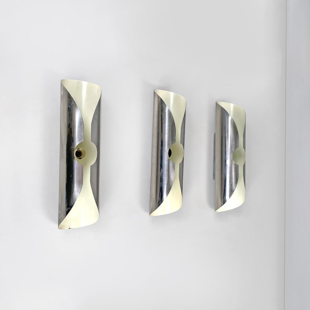 Italian modern chromed metal and white cylindrical wall lamps, 1970s
Set of three cylindrical wall lamps in chromed metal, with white lacquering inside. They have an elongated shape, the structure is composed of a single metal plate that folds on