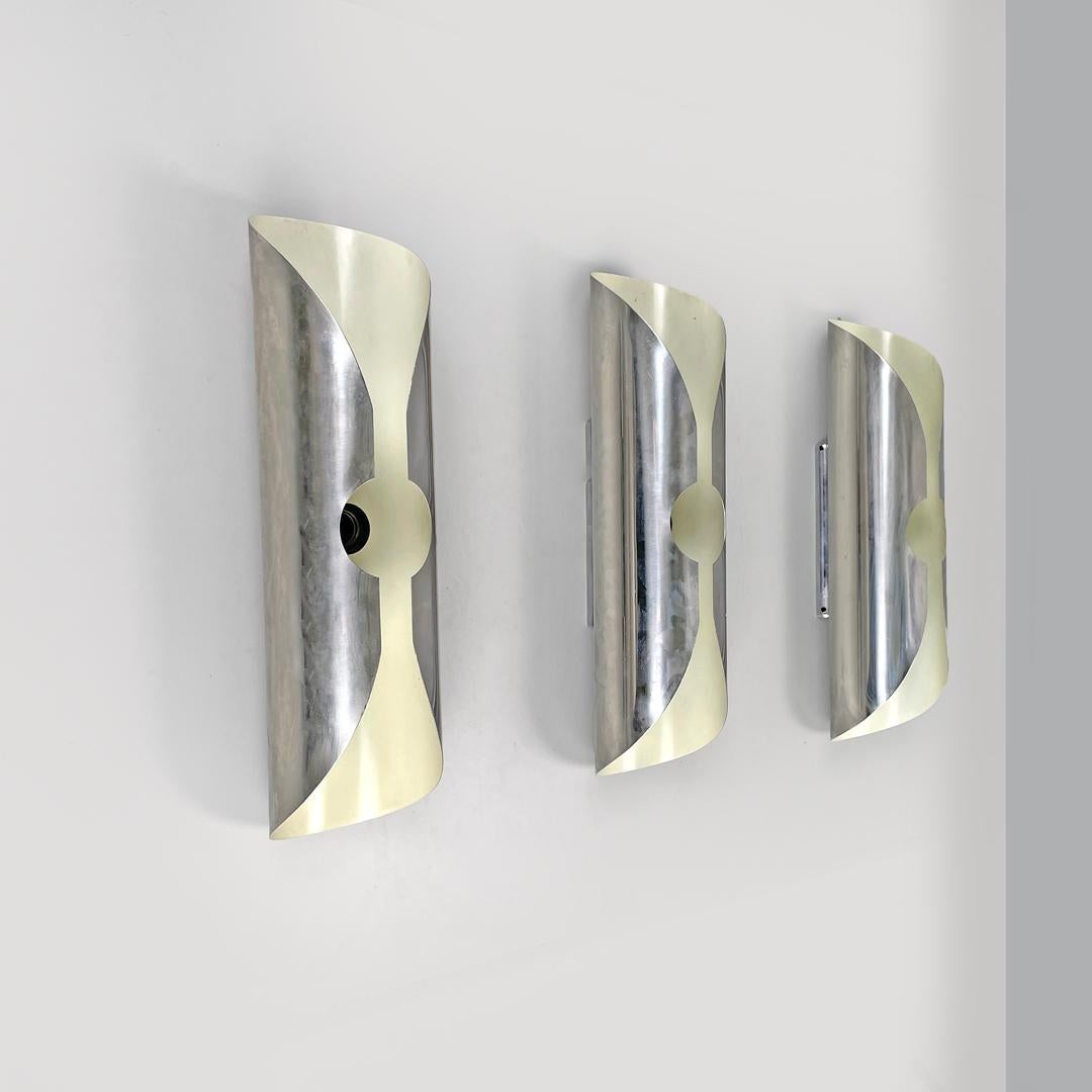 Italian modern chromed metal and white cylindrical wall lamps, 1970s
Set of three cylindrical wall lamps in chromed metal, with white lacquering inside. They have an elongated shape, the structure is composed of a single metal plate that folds on