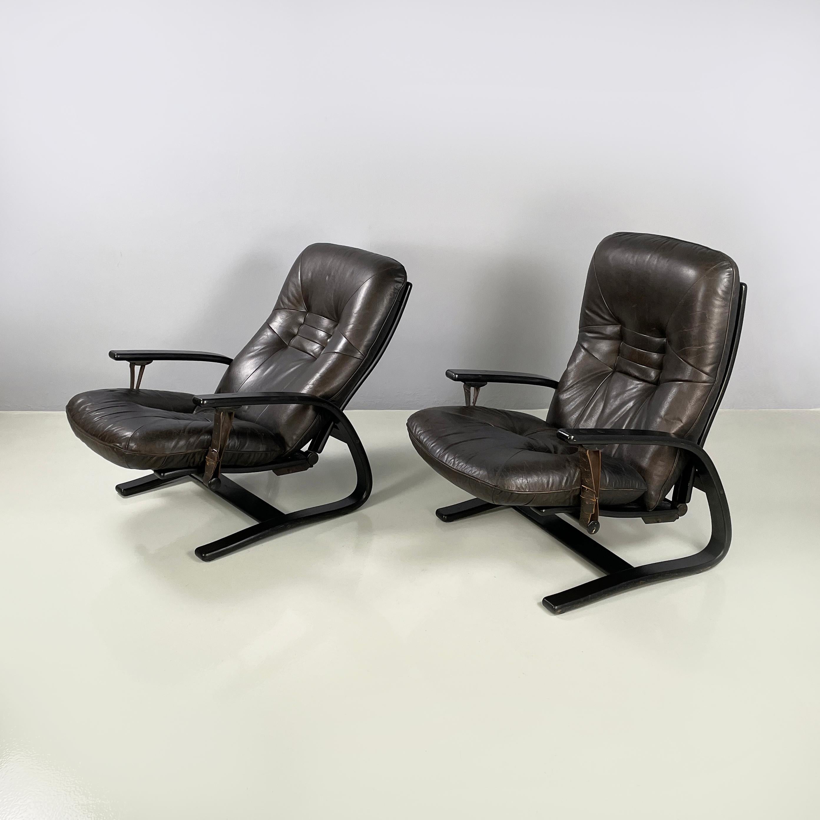 Italian modern Dark brown leather Reclining armchairs and pouf by De Sede, 1970s
Pair of reclining armchairs and pouf in dark brown leather and dark wood. The square back and seat are padded and covered in dark brown leather and feature buttons with