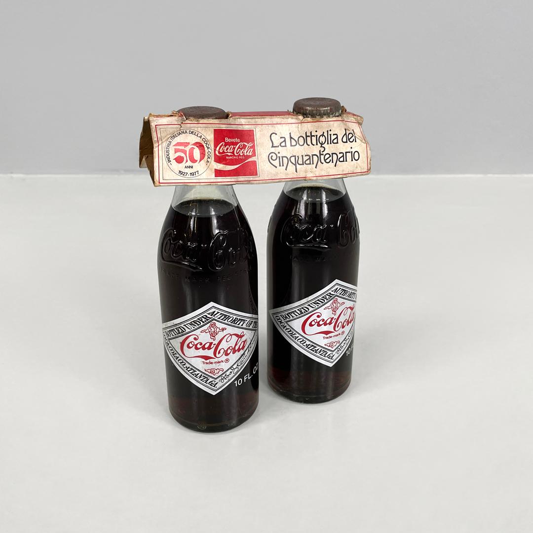 Bottiglie italiane moderne per il cinquantesimo anniversario della Coca-Cola, 1977
Coppia di bottiglie di Coca-Cola in vetro con bevanda, le bottiglie sono intatte. Le due bottiglie sono unite da una confezione di carta che le tiene