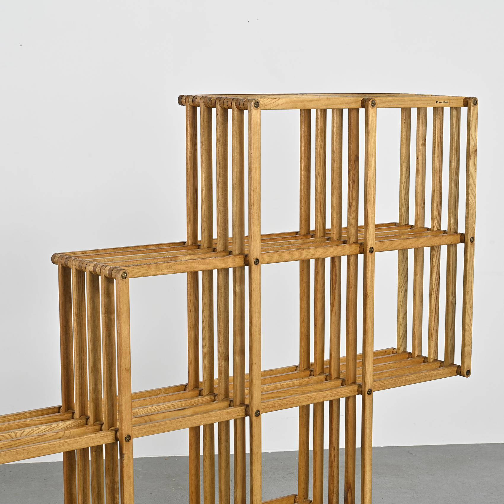 Crafted in the 1980s, this Italian modern wooden folding floor and wall bookcase by Pool Shop stands out with its irregular design. Boasting 11 square compartments and an external shelf, its unique structure is entirely collapsible, facilitated by