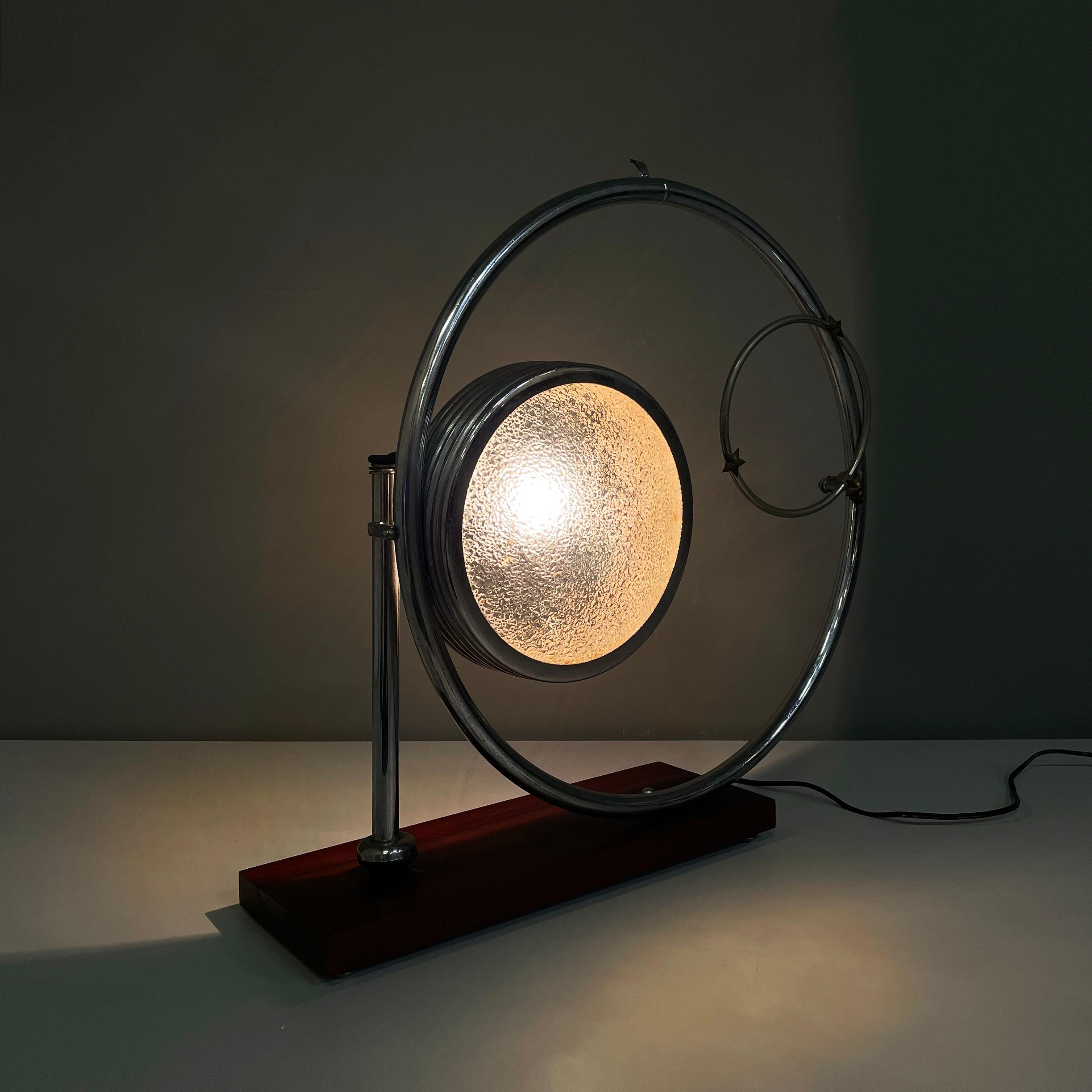 Italian modern Geometrical table lamp with crafted glass, metal and wood, 1980s
Geometrical table lamp with rectangular base in dark wood. The round diffuser is made of finely worked glass with thick metal profiles. The structure that supports the