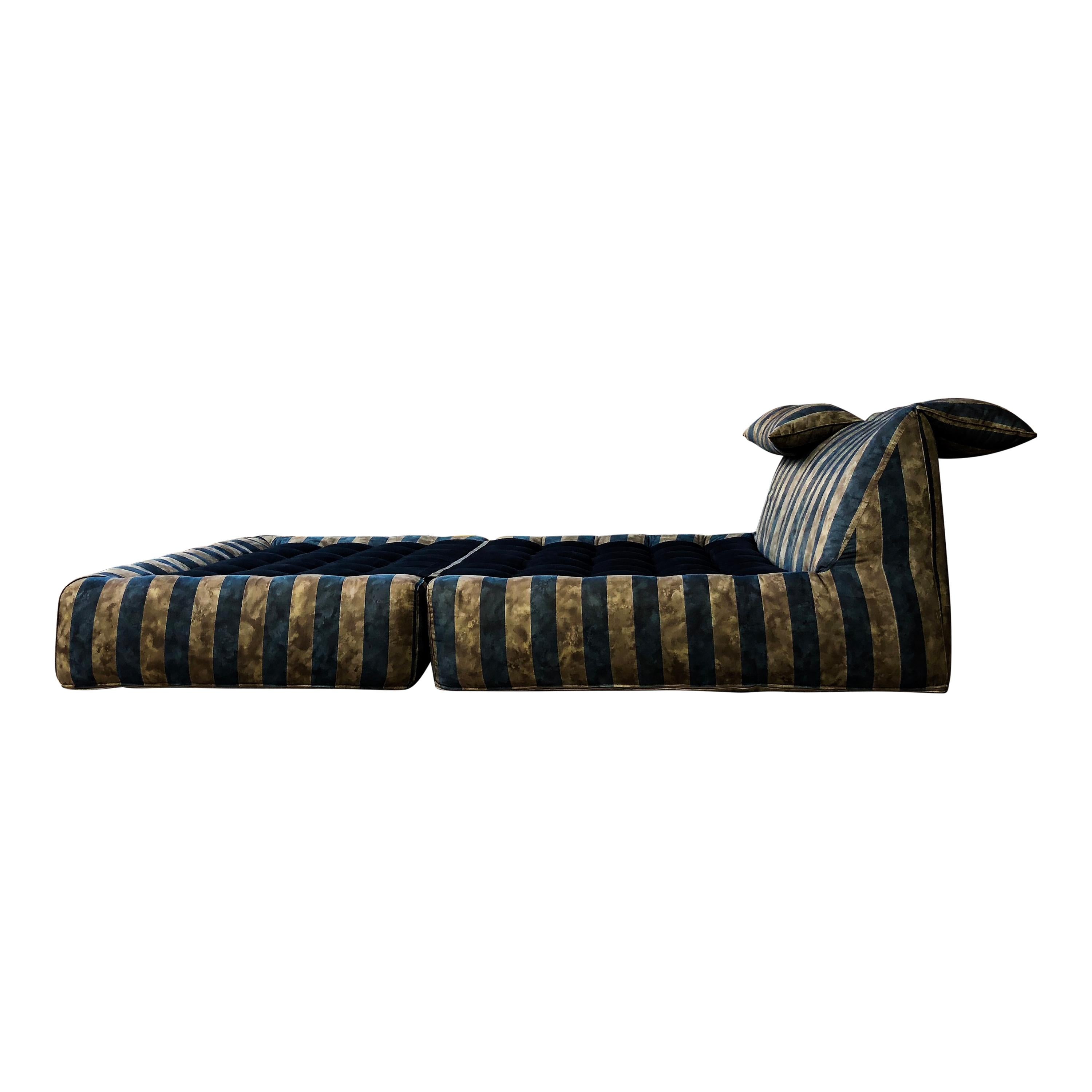 This Le Bambole day bed was designed by Mario Bellini in 1972 and manufactured by B&B Italia in 1976. It features a tubular steel structure, polyurethane foam, and a blue and beige striped upholstery (with a particular pattern that gives it a satin
