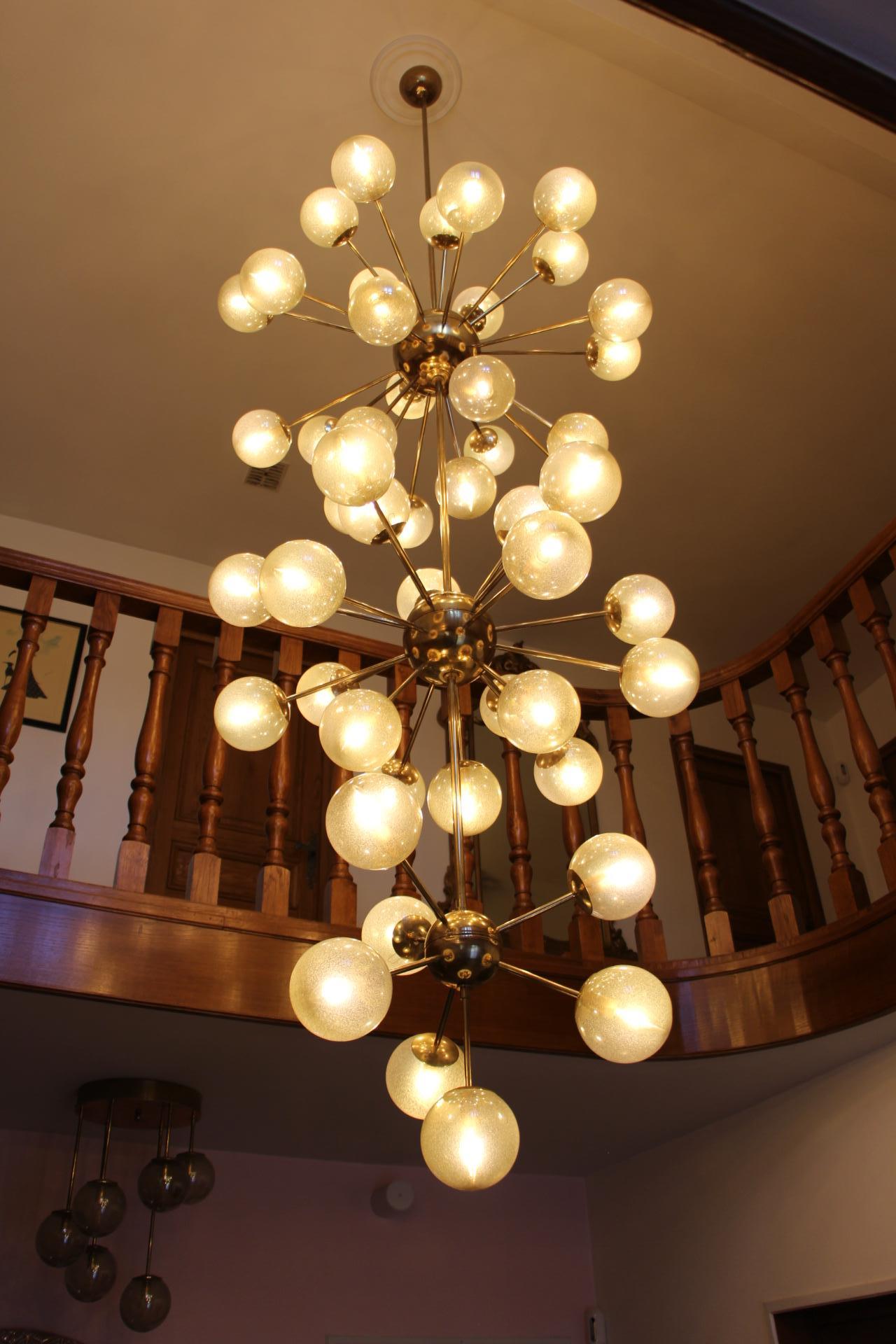 This spectacular three tiers brass chandelier is absolutely gorgeous with its 50-light and its champagne-golden blown glass globes. Its globes feature thousands of little bubbles inside the glass.Each one has been made individually, by hand in