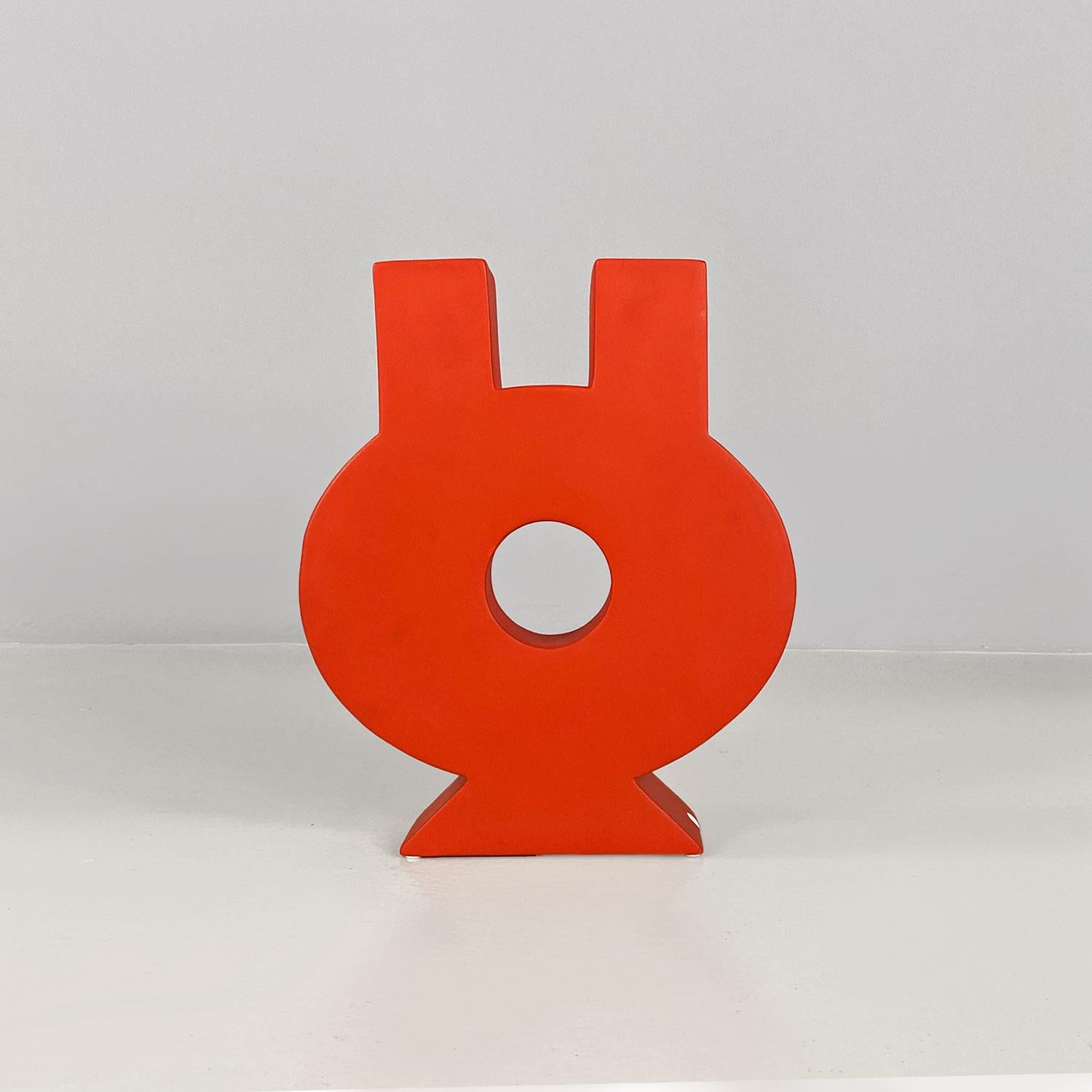 Keramische Skulptur in leuchtendem Rot mit mattem Finish. Der Gegenstand der Skulptur ist geometrisch und rund, mit einem runden Loch in der Mitte und zwei quadratischen Öffnungen im oberen Teil. Die Skulptur kann auch als Vase verwendet