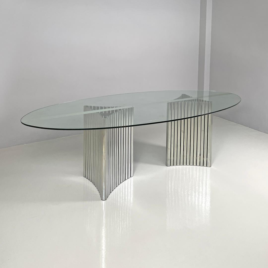 Italian modern oval glass top dining table with chromed metal columns, 1970s
Dining table with oval glass top with central silver decorative band. The legs are two chromed metal columns composed of many vertical strips, which follow a triangular