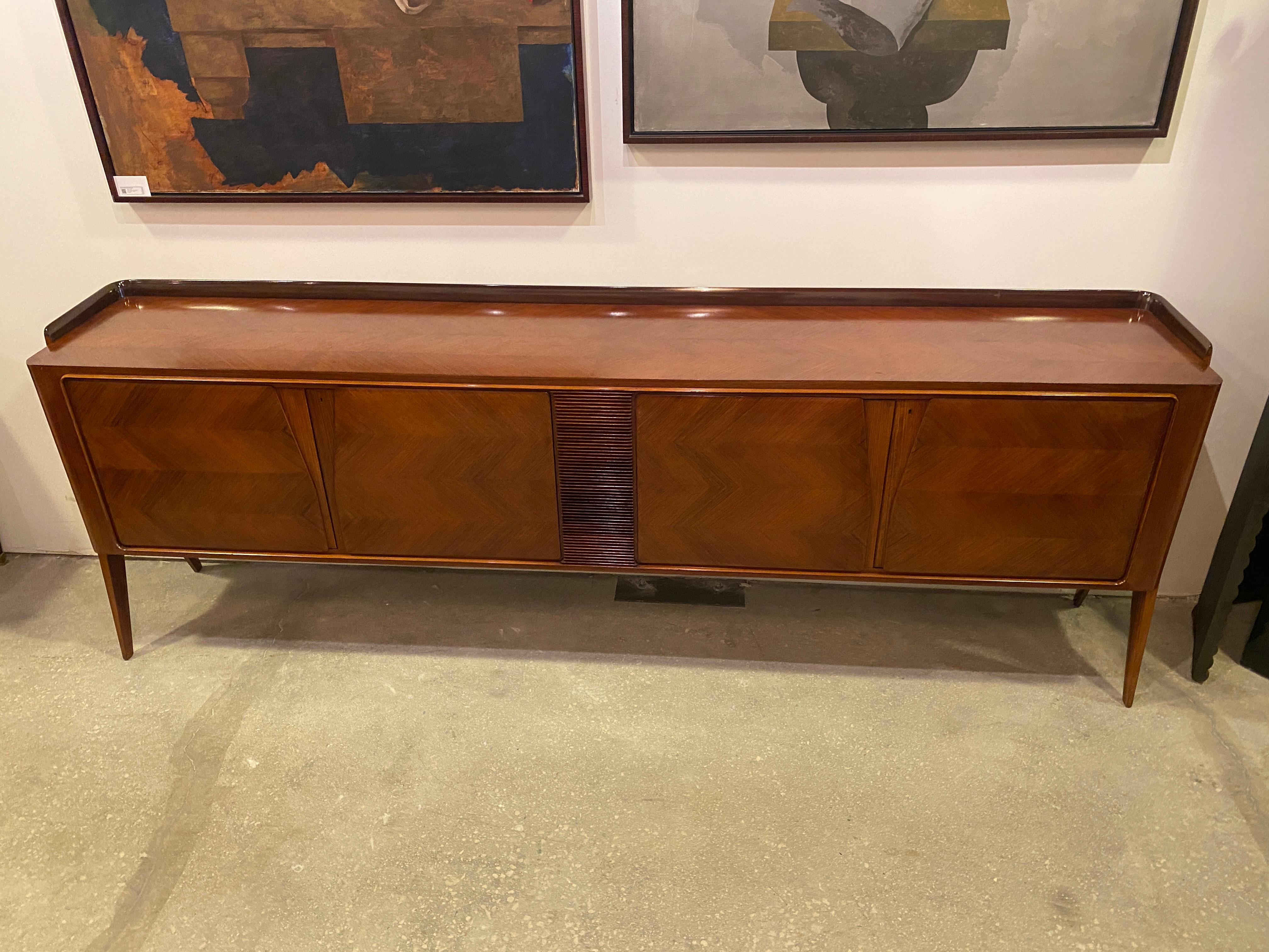 This four door credenza has fine herringbone parquetry displayed on both sets of doors, separated by a faux louvered partitian. The four doors open to ample cabinet space on both sides with a set of shelves included. The top has a raised gallery on