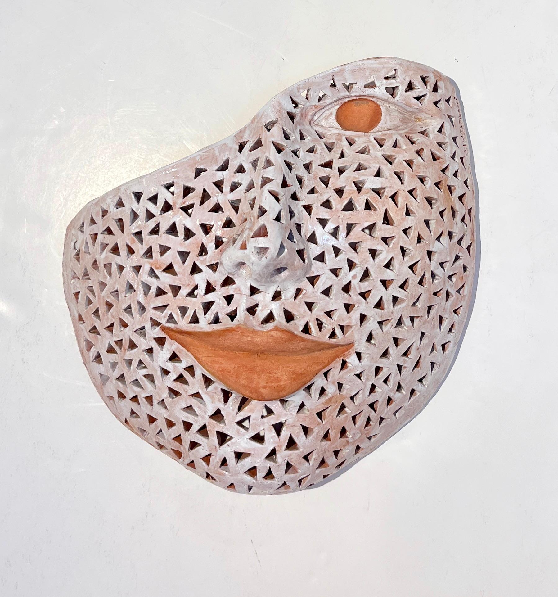 Contemporary sculpture in terra cotta in the shape of a feminine mask, handcrafted with a pierced decoration and white brush painted with fired enamel. This wall decoration has a special uniqueness because of the diffused aura created by the light