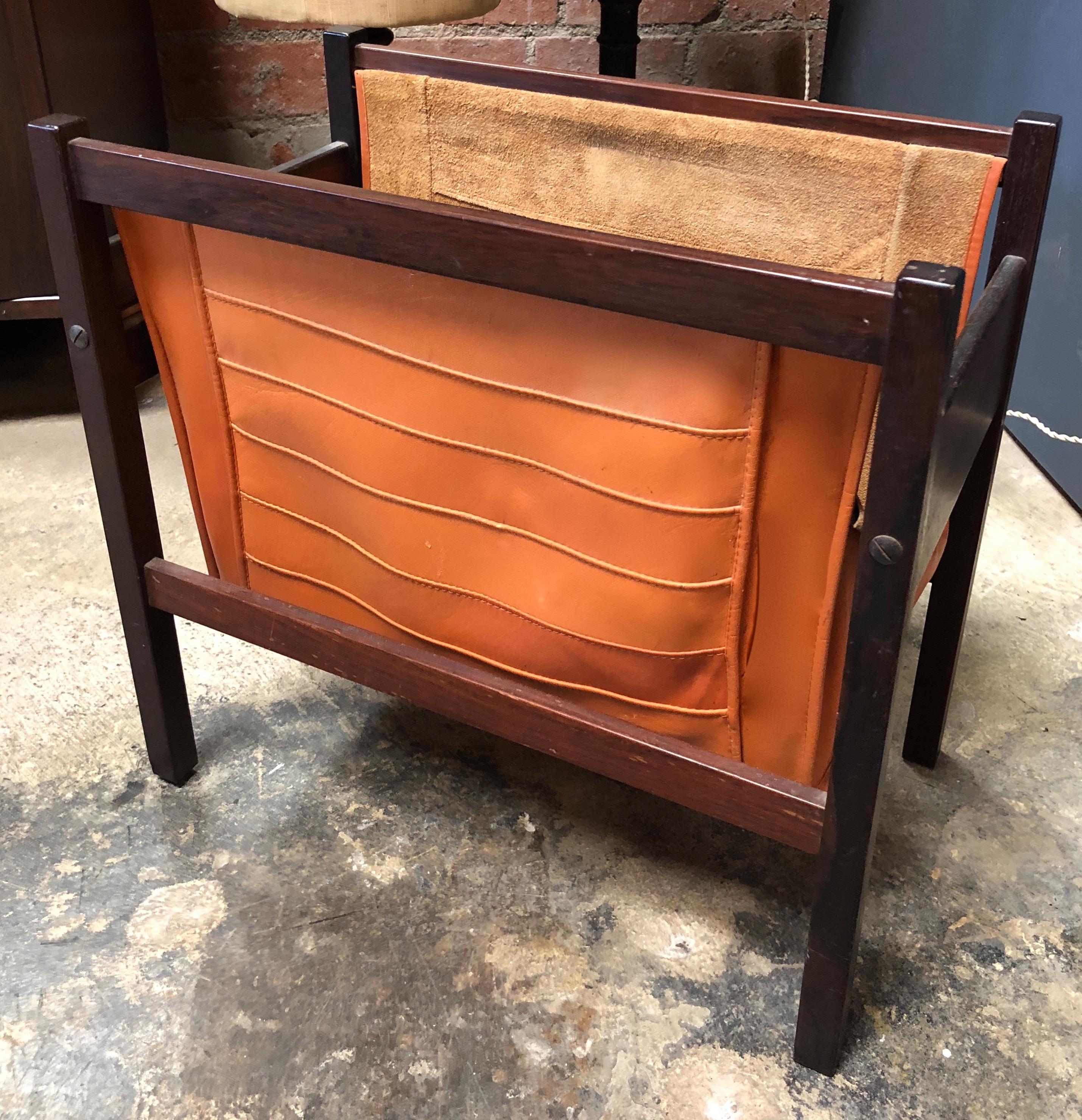 This is a very nice Italian modern teak and dark orange leather magazine rack . The 1960s era Minimalist design has two sling compartments that are connected by wide visible straight line .This lovely quality Danish modern rosewood magazine rack has