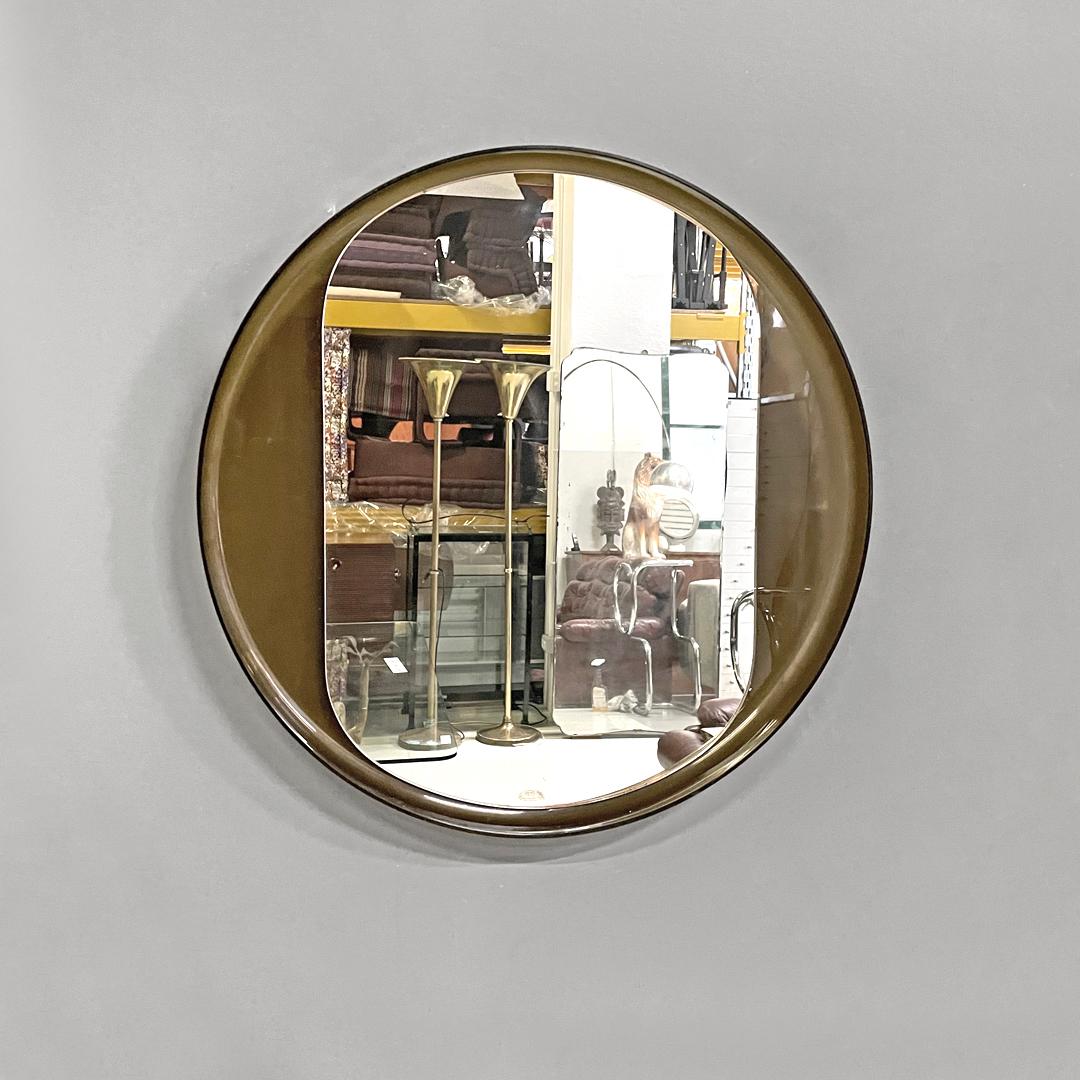 Italian modern round wall mirror in semitransparent brown plastic, 1970s 
Round wall mirror. It has a brown semi-transparent plastic structure with raised edges, which contains an oval mirror in the centre. Being semi-transparent, the color of the