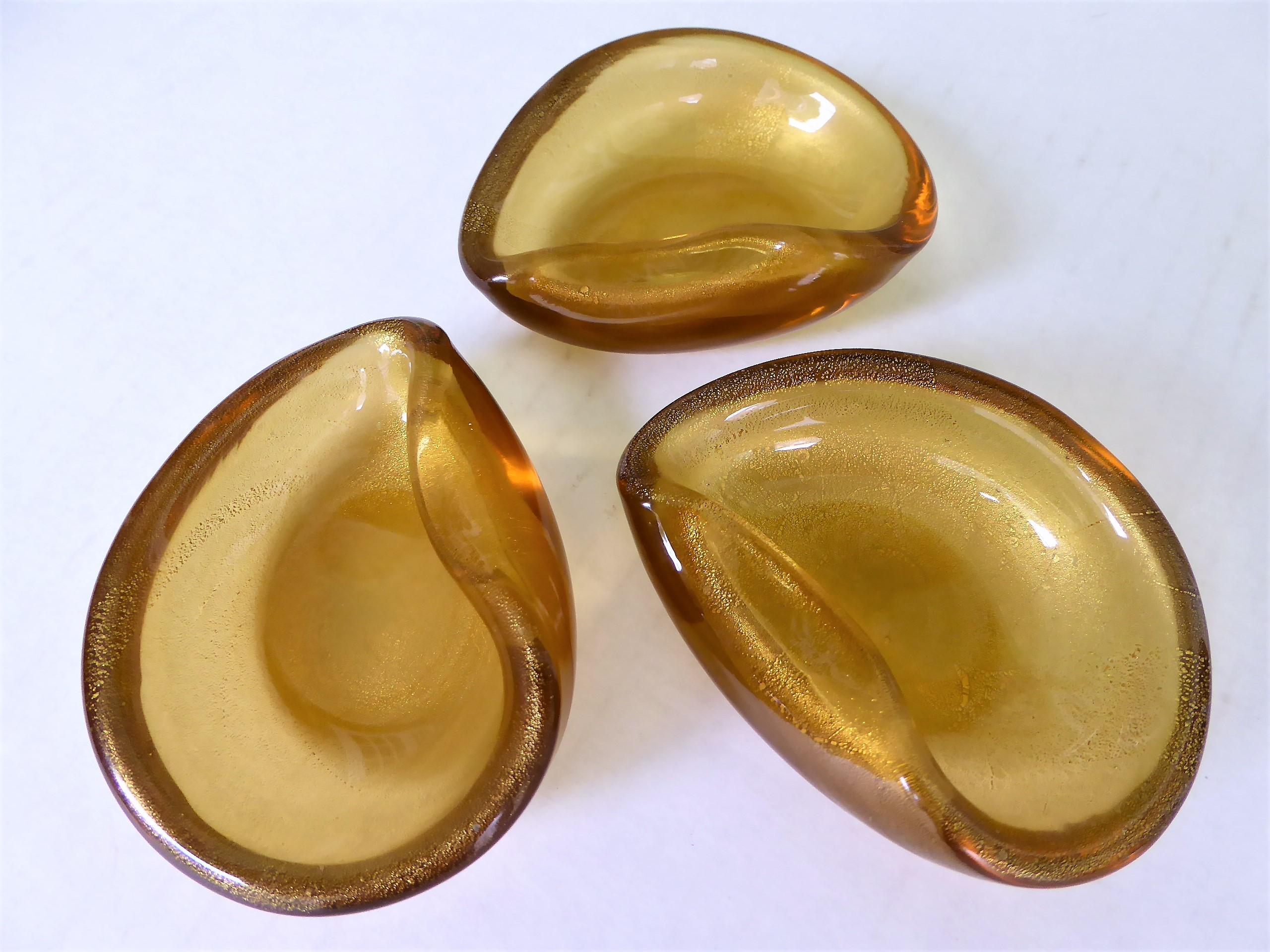 Wonderful Murano creations. Three clam shell or ear shaped vessels of blown glass with gold leaf inclusions. Wonderfully blown and shaped. For use as salt cellars or originally probably as small individual ashtrays.

Measurements each: 3 1/2