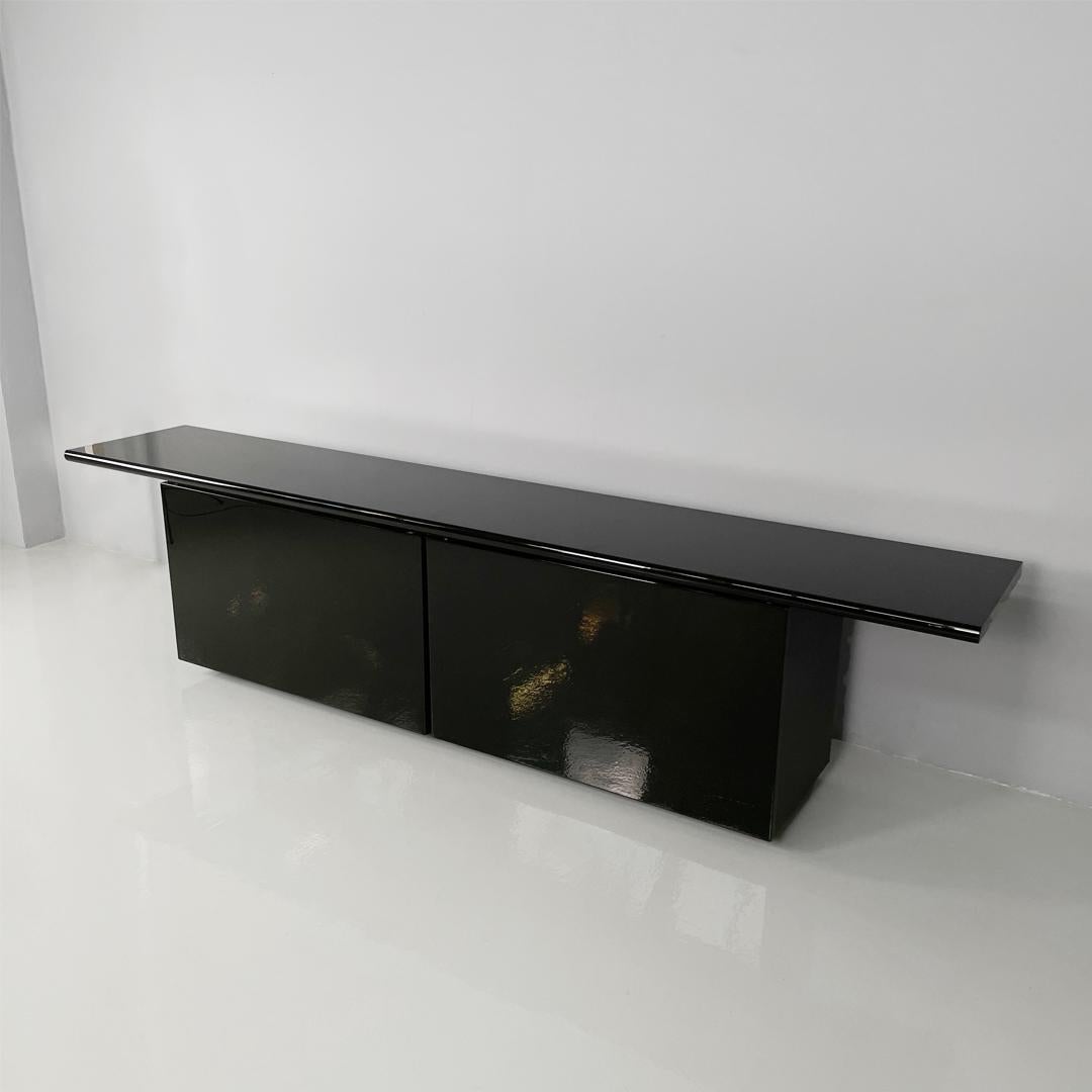 Sheraton model sideboard, with structure entirely in glossy black lacquered wood. The rectangular top has a beveled front edge, on the front there is a row of four black wooden drawers and three compartments with glass shelves and chromed metal
