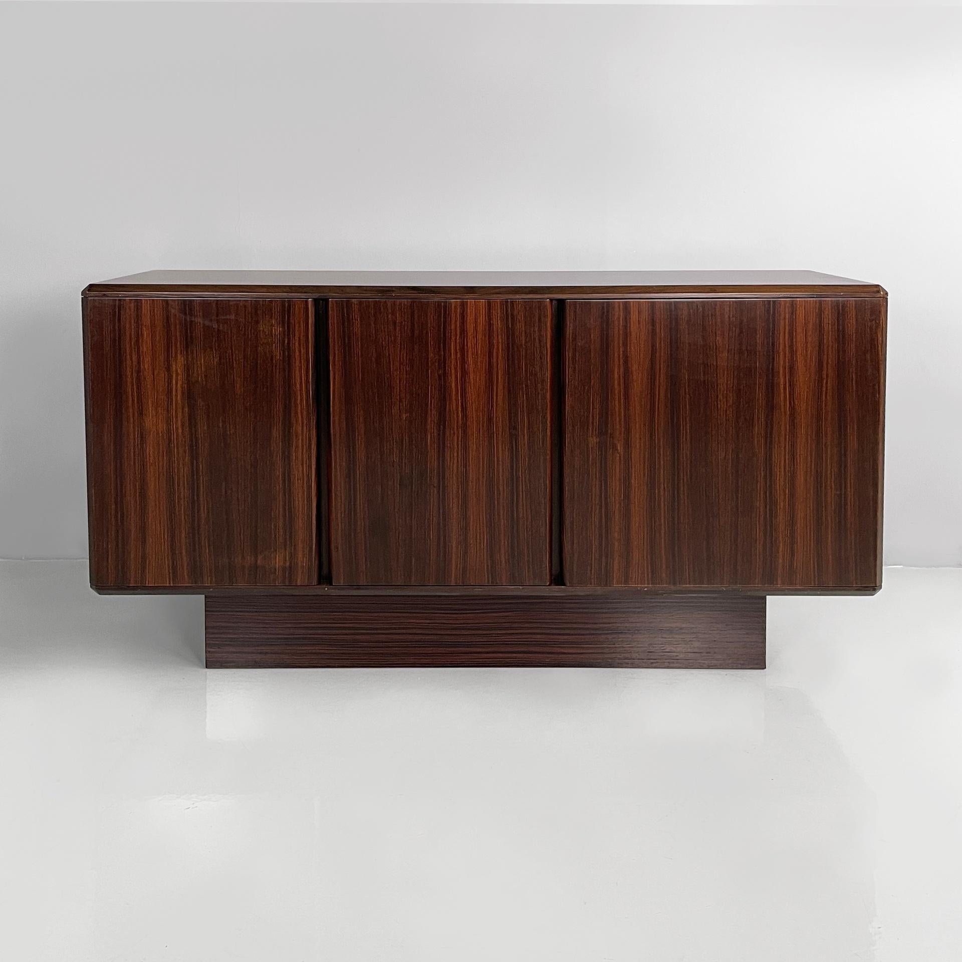 Italian modern sideboard in wood with hinged doors, shelves and drawers, 1970s
Rectangular sideboard made entirely of dark wood. The front features two compartments: one with a hinged door and an internal shelf and the other with a double hinged