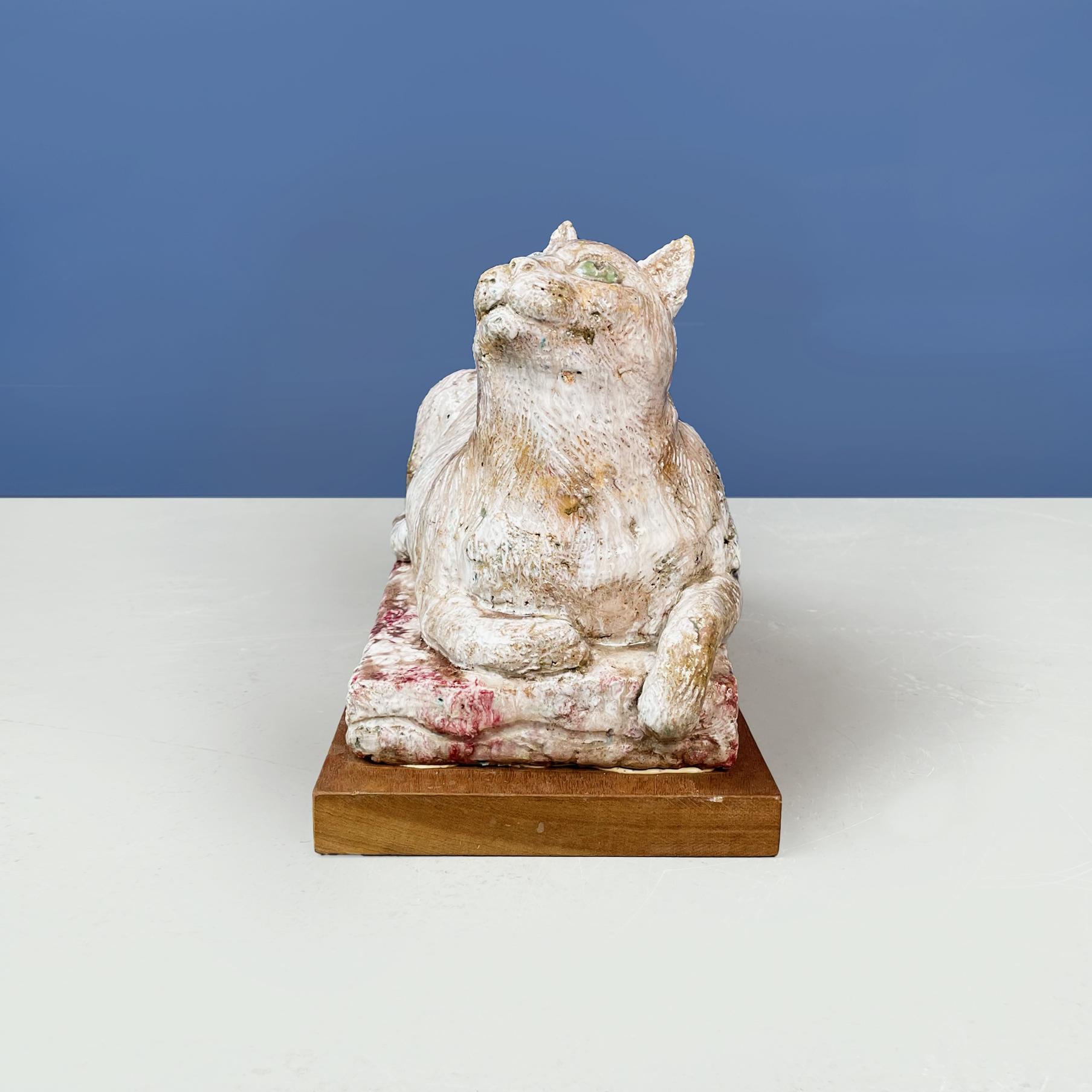 Italian modern Statue of cat in red and white terracotta by M. Moretto, 1980s
Statue of cat lying down looking upwards, in withe soft pink and red painted terracotta. 
The cat's eyes are green. Finely crafted. Wooden base.
Produced by M. Moretto in
