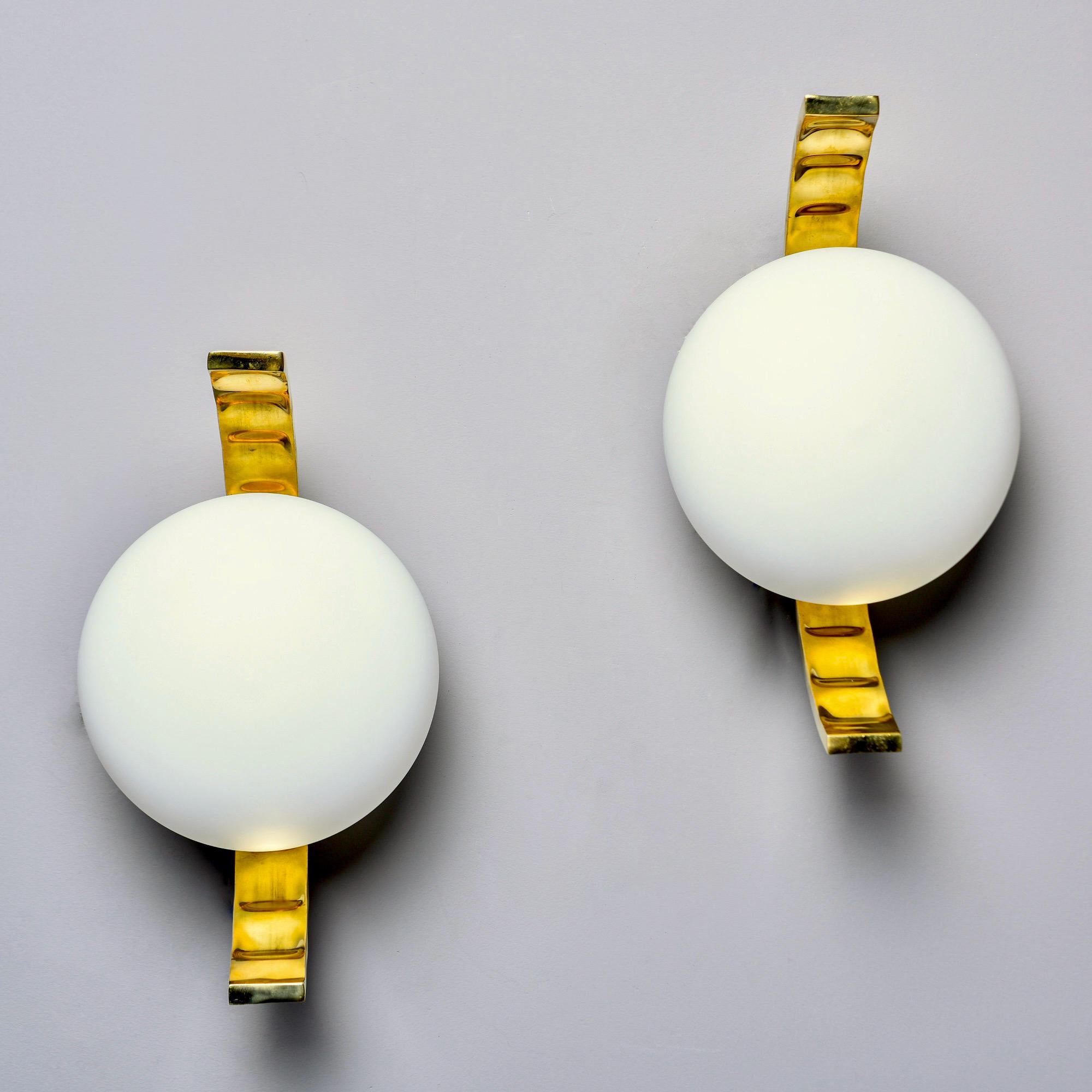 New and made in Italy, these Mid-Century Modern style sconces have a distinct profile with curved polished brass frames and a white glass globe center. Wired for US electrical standards. Sold and priced as a pair.