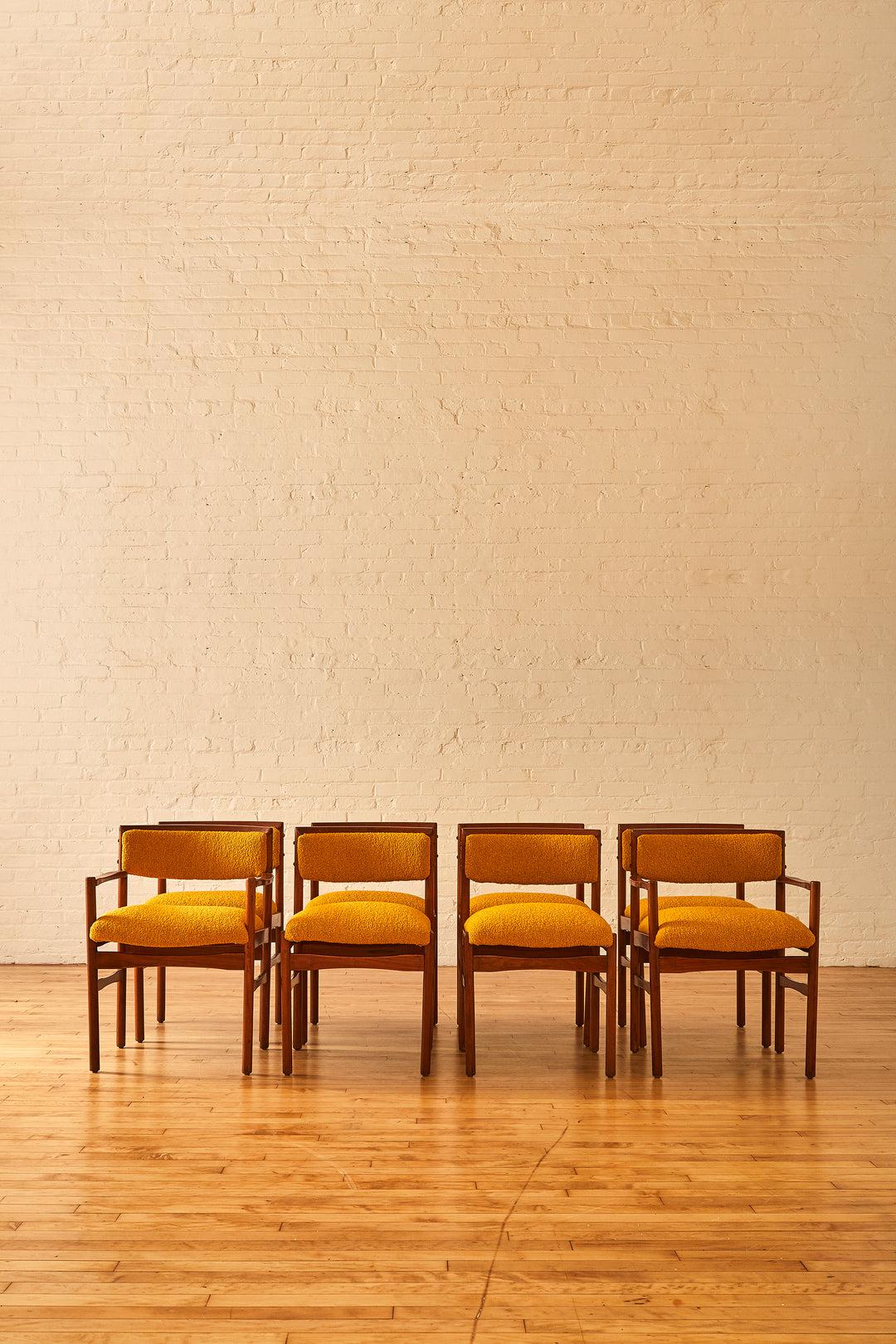 A set of 8 Italian modern teak dining chairs with gently curved backs and prominent patina on the wood. These chairs have been professionally reupholstered and refinished with a wool & cotton boucle in a mustard yellow. The set features two